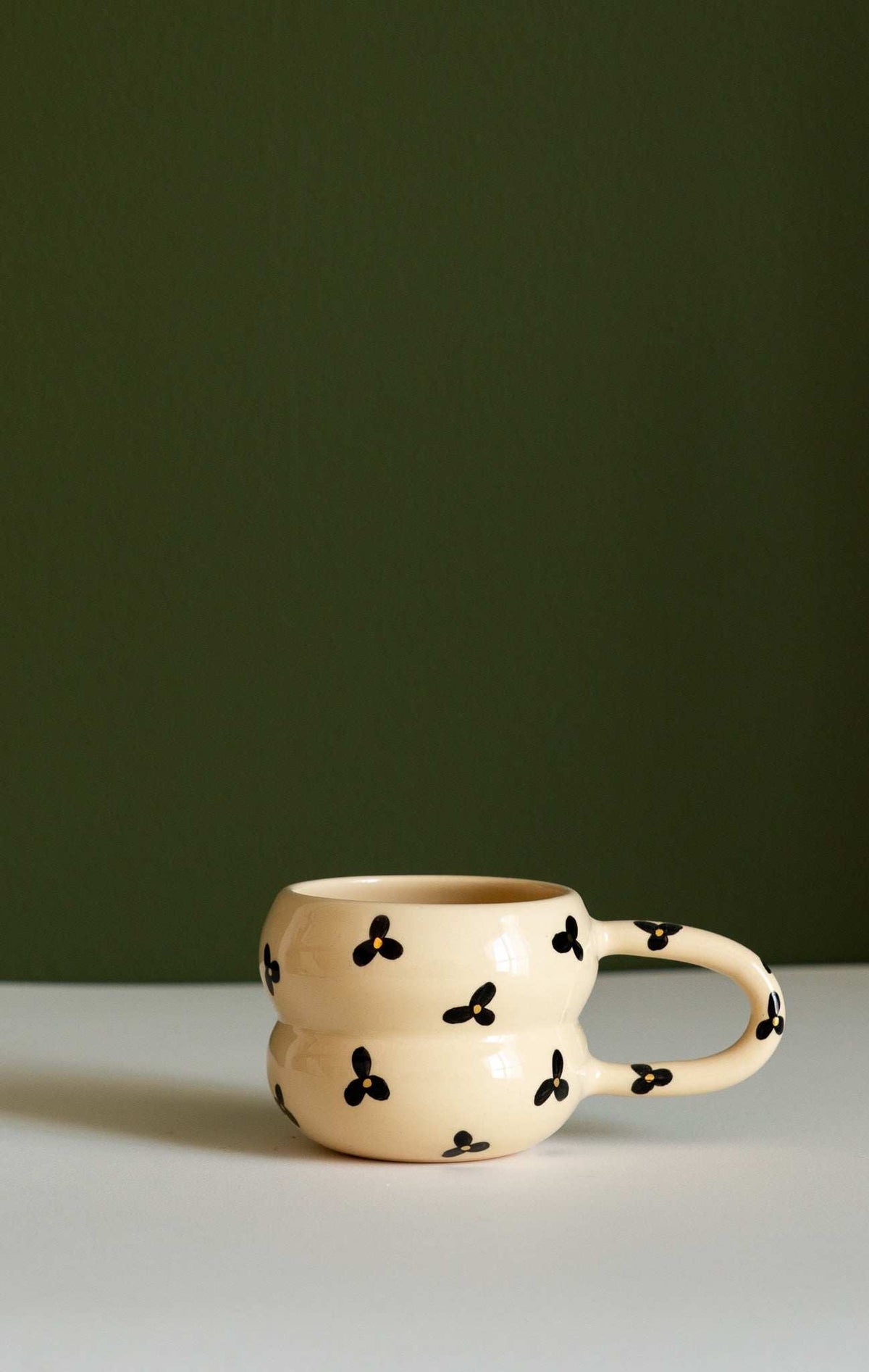 Bubble Mug in cream ceramic with a sculpted double-ring shape, black three-petal flowers, and a rounded handle.