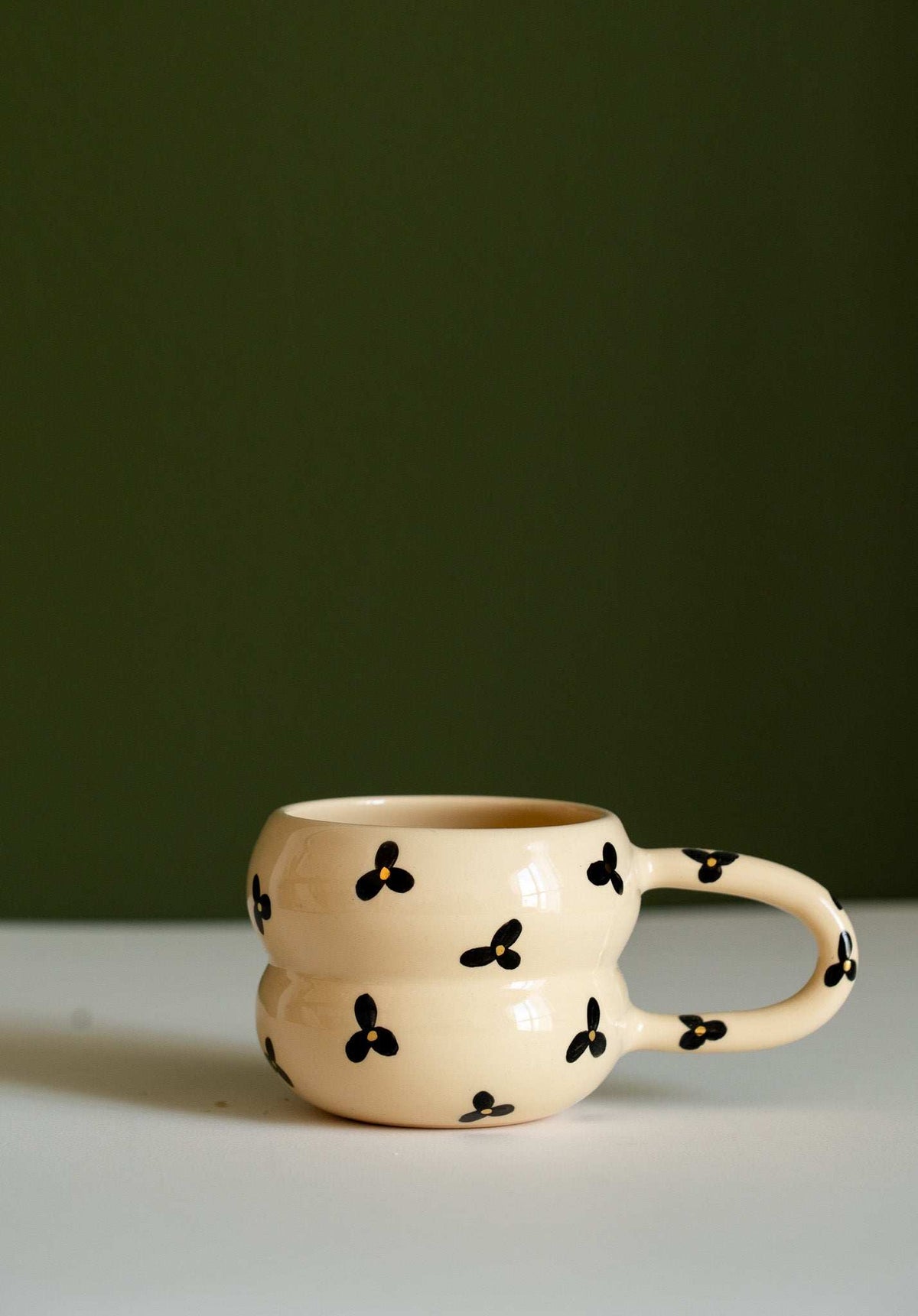Bubble Mug in cream ceramic with black three-petal flowers and yellow centers, sculpted double-ring shape and loop handle.