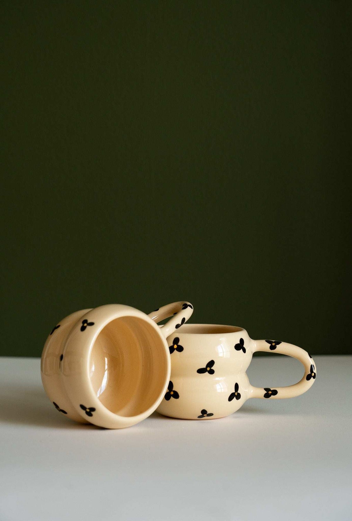 Bubble Mug in cream ceramic with black three-petal floral pattern, sculptural double-ring body and curved handle.