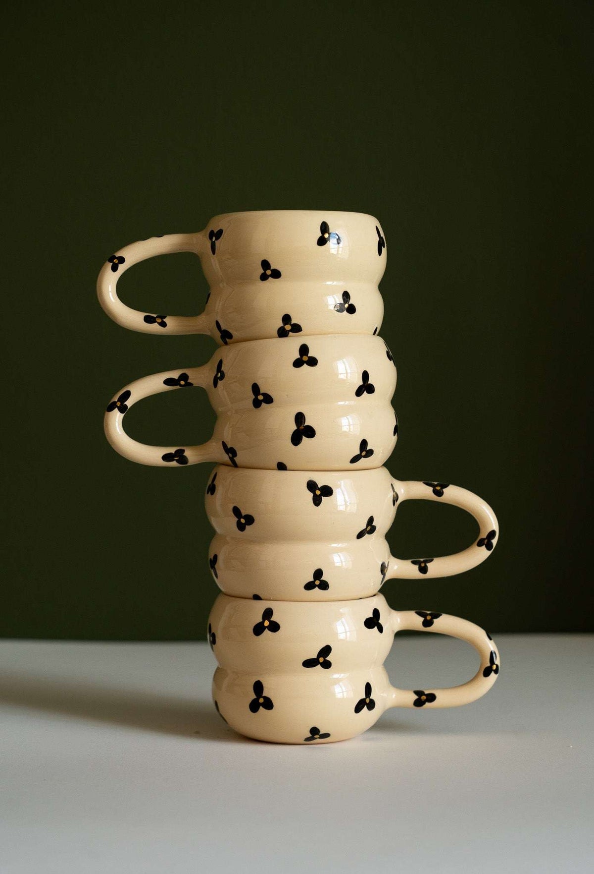 Bubble Mug made of cream-colored ceramic, with a glossy finish, stacked rounded rings, and black floral motifs with yellow centers.