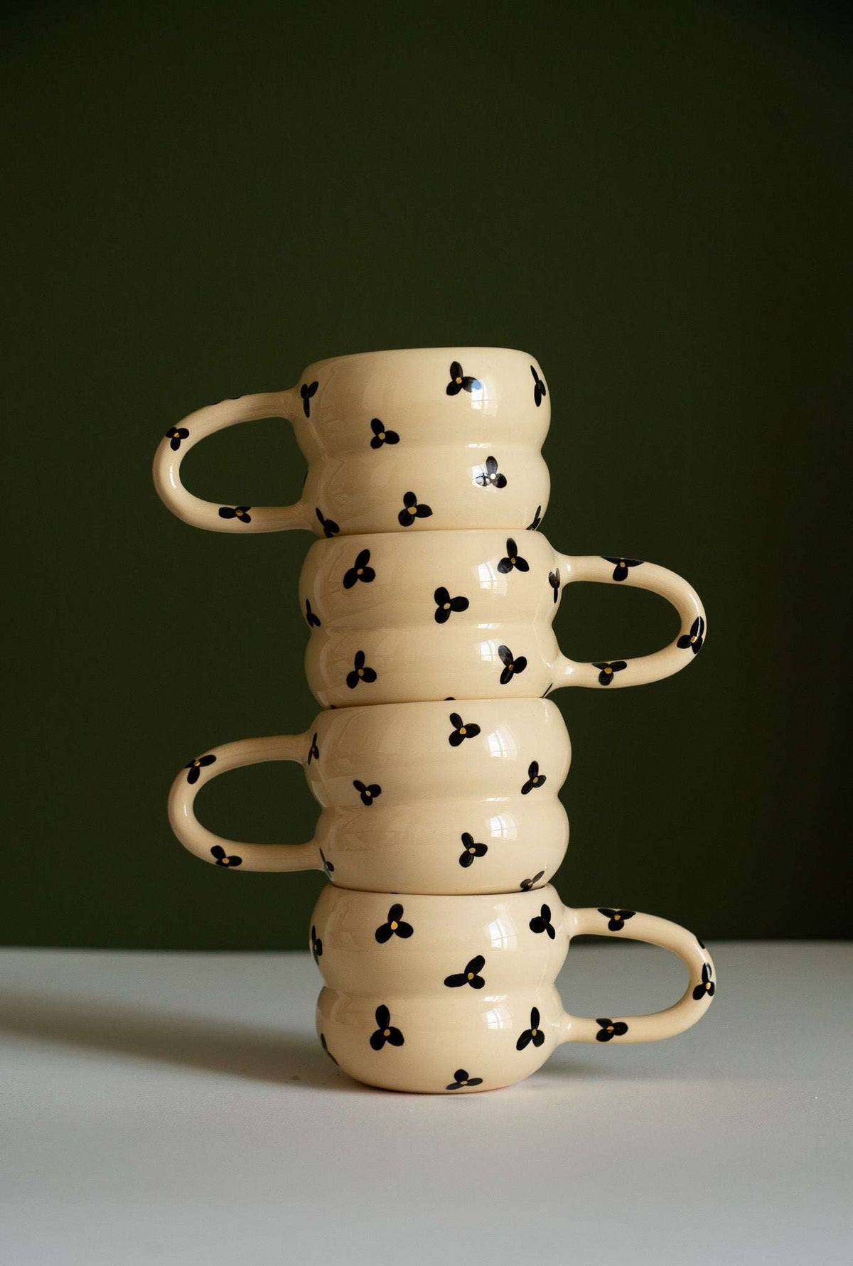 Bubble Mug in cream ceramic with glossy glaze, black three-petal flowers and yellow centers, sculpted rings and loop handle.