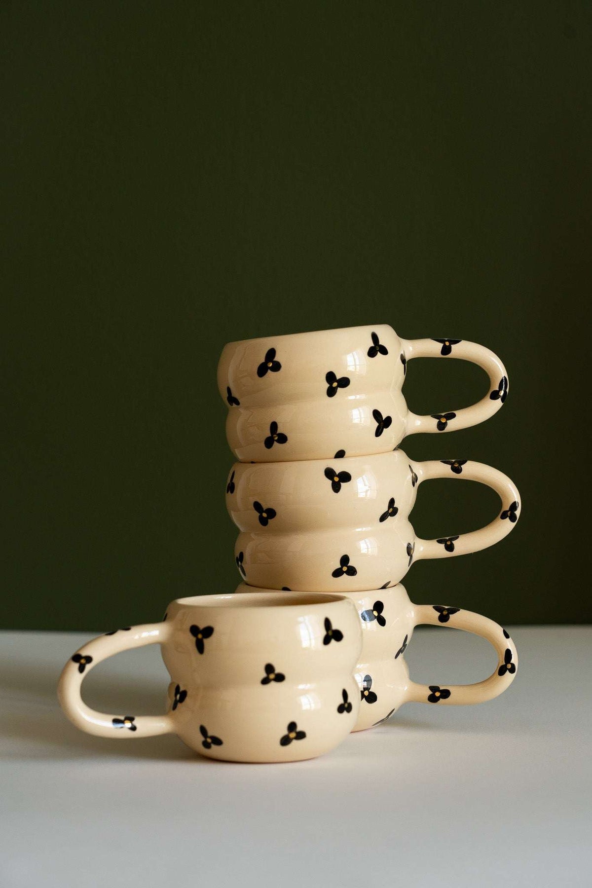 Bubble Mug in glossy cream ceramic with black three-petal flowers and a rounded, double-ring shape with curved handle.