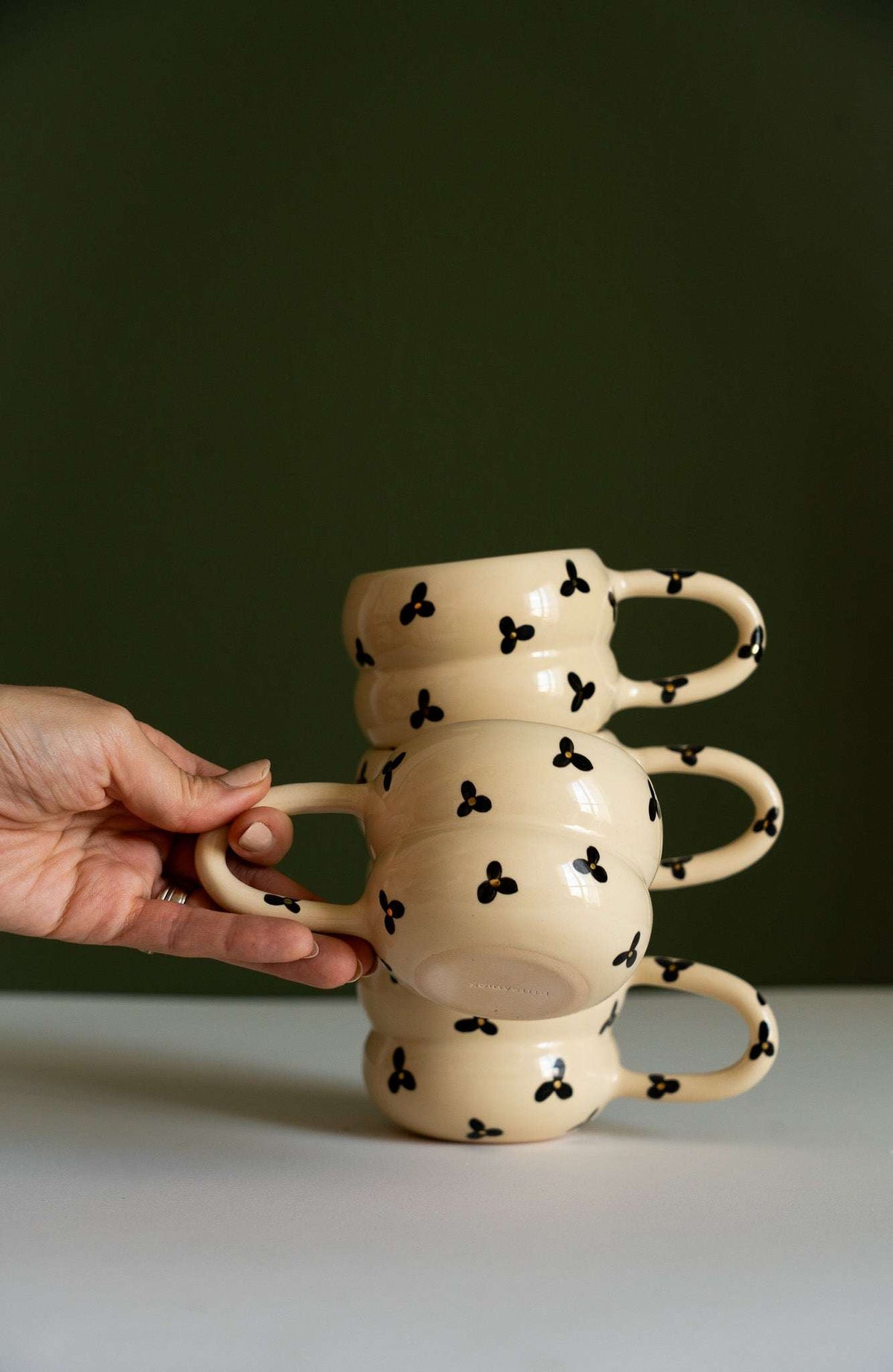 Bubble Mug in glossy cream ceramic, with a sculptural stacked bubble shape, looping handles, and black floral motifs with yellow centers.