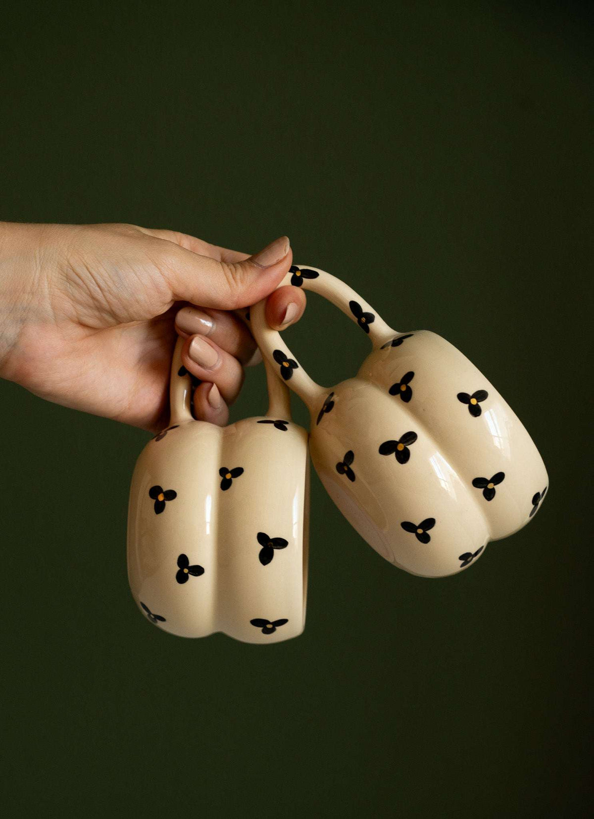 Bubble Mug with a glossy cream ceramic double-ring shape, black three-petal flowers, yellow centers, and a floral handle