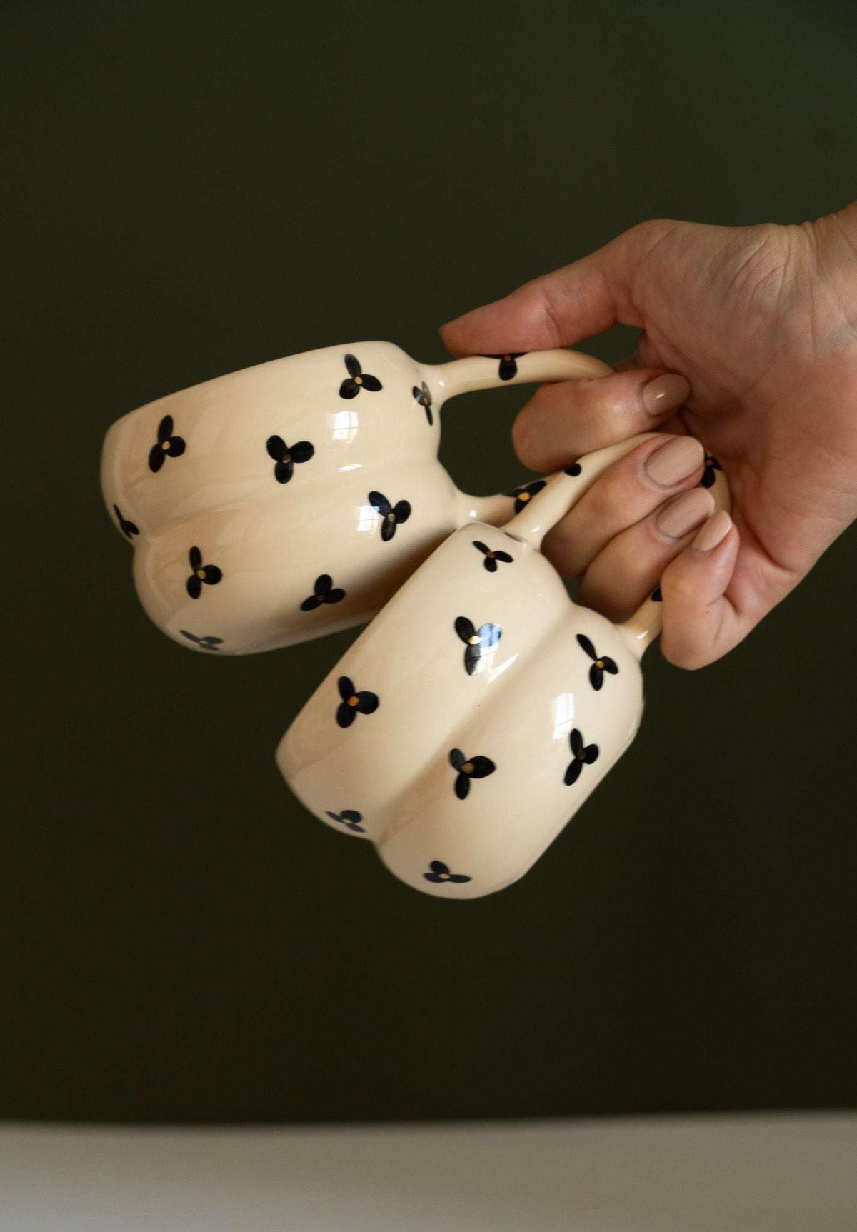 Bubble Mug in glossy cream ceramic, with black three-petal flowers and yellow centers, double-ring shape and floral handle.
