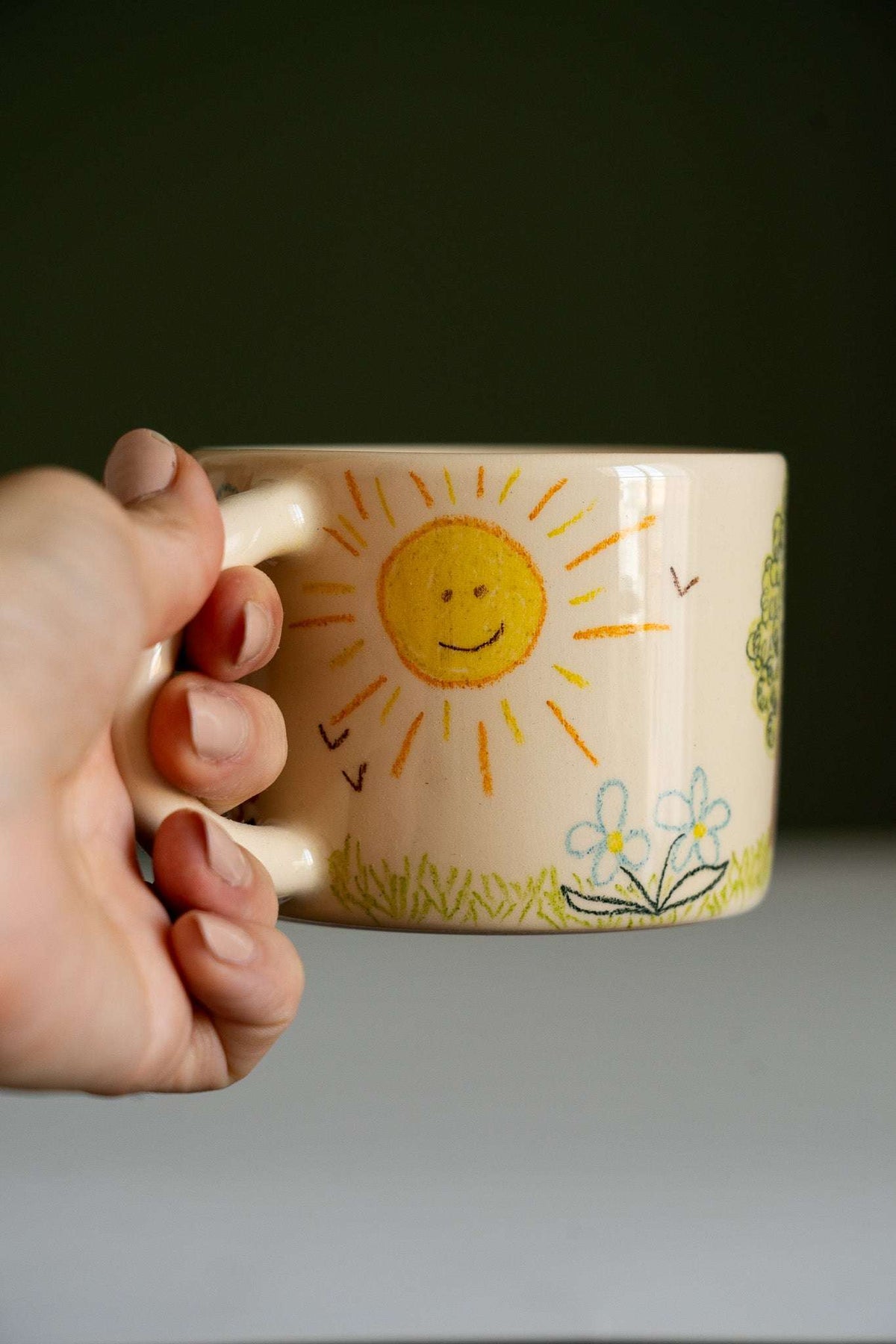 Kids Artwork Stoneware Mug in beige ceramic with a smiling yellow sun, flowers, birds, and crayon-style landscape art.