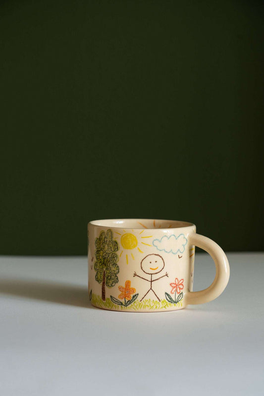 Kids Artwork Stoneware Mug in beige ceramic, with a rounded handle and colorful hand-drawn sun, trees, flowers and figure.