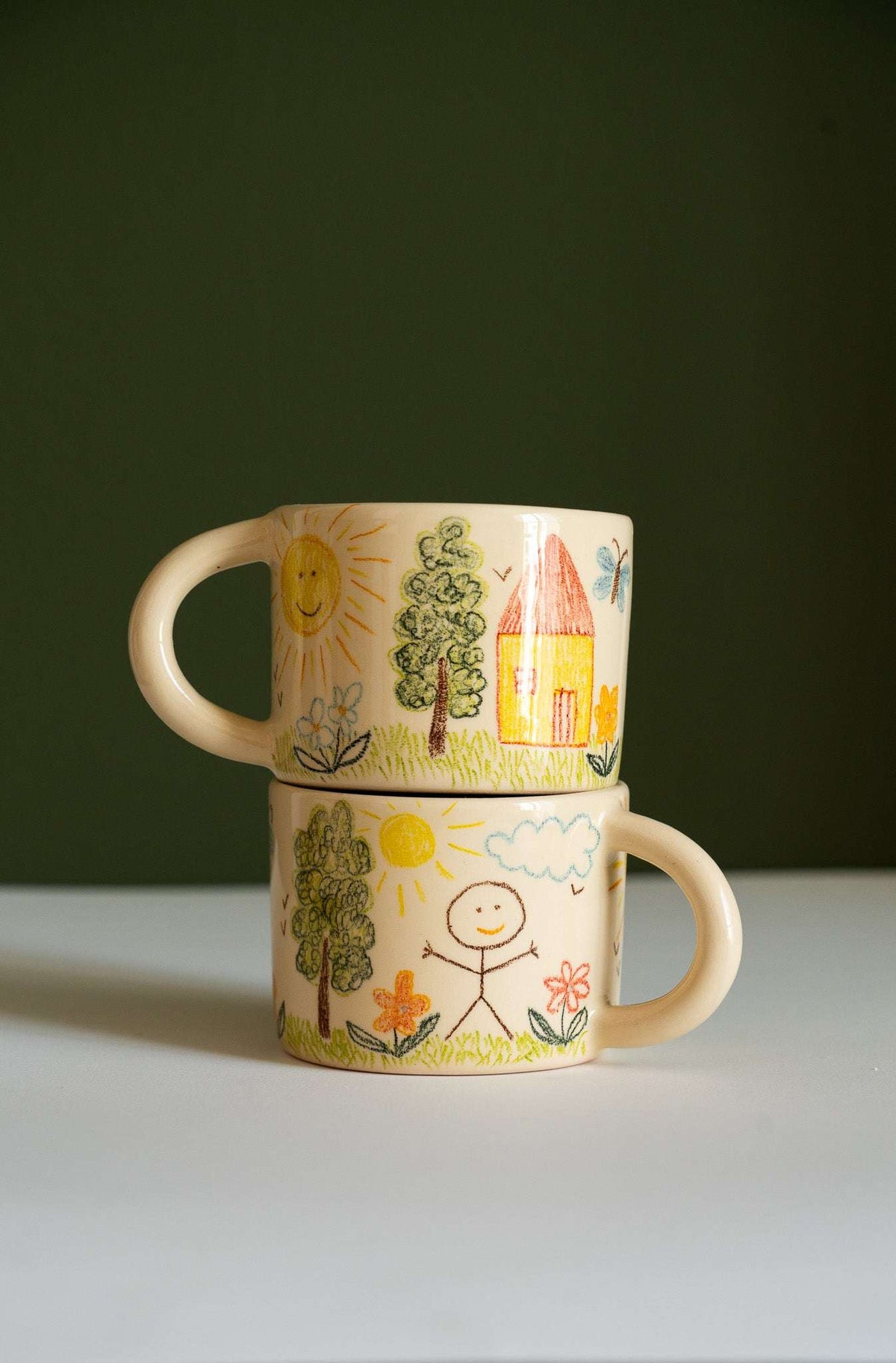 Kids Artwork Stoneware Mug in beige ceramic, decorated with colorful childlike drawings of suns, trees, flowers, and a smiling figure.