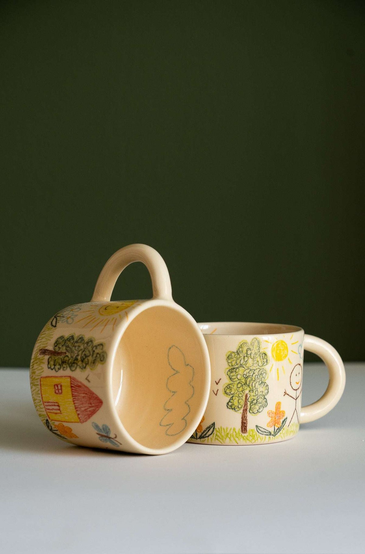 Kids Artwork Stoneware Mug in beige ceramic, with a playful hand-drawn landscape, smiling sun, trees, flowers, and rounded handle.