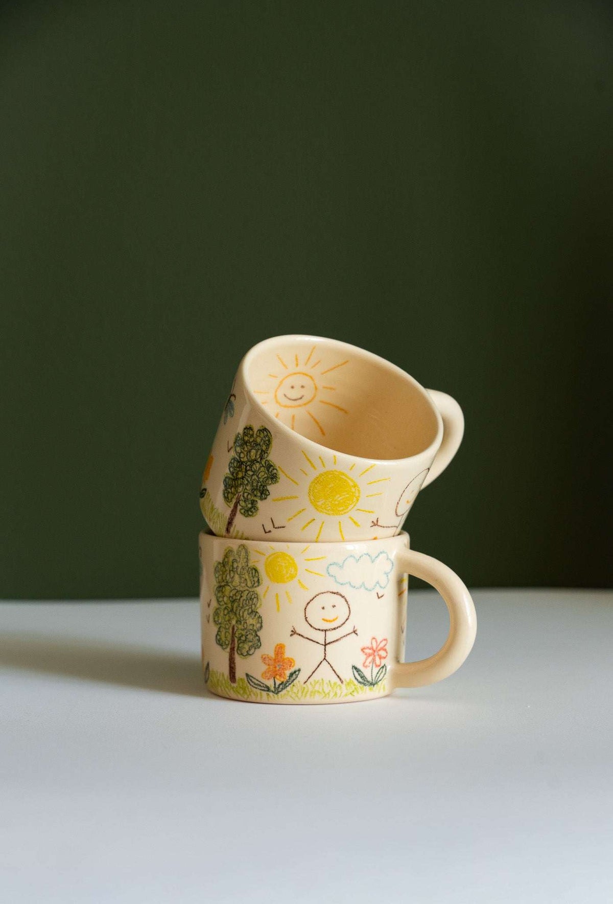 Kids Artwork Stoneware Mug in beige ceramic with a glossy glaze, hand-drawn suns, trees, flowers, birds and stick figures, rounded handle.
