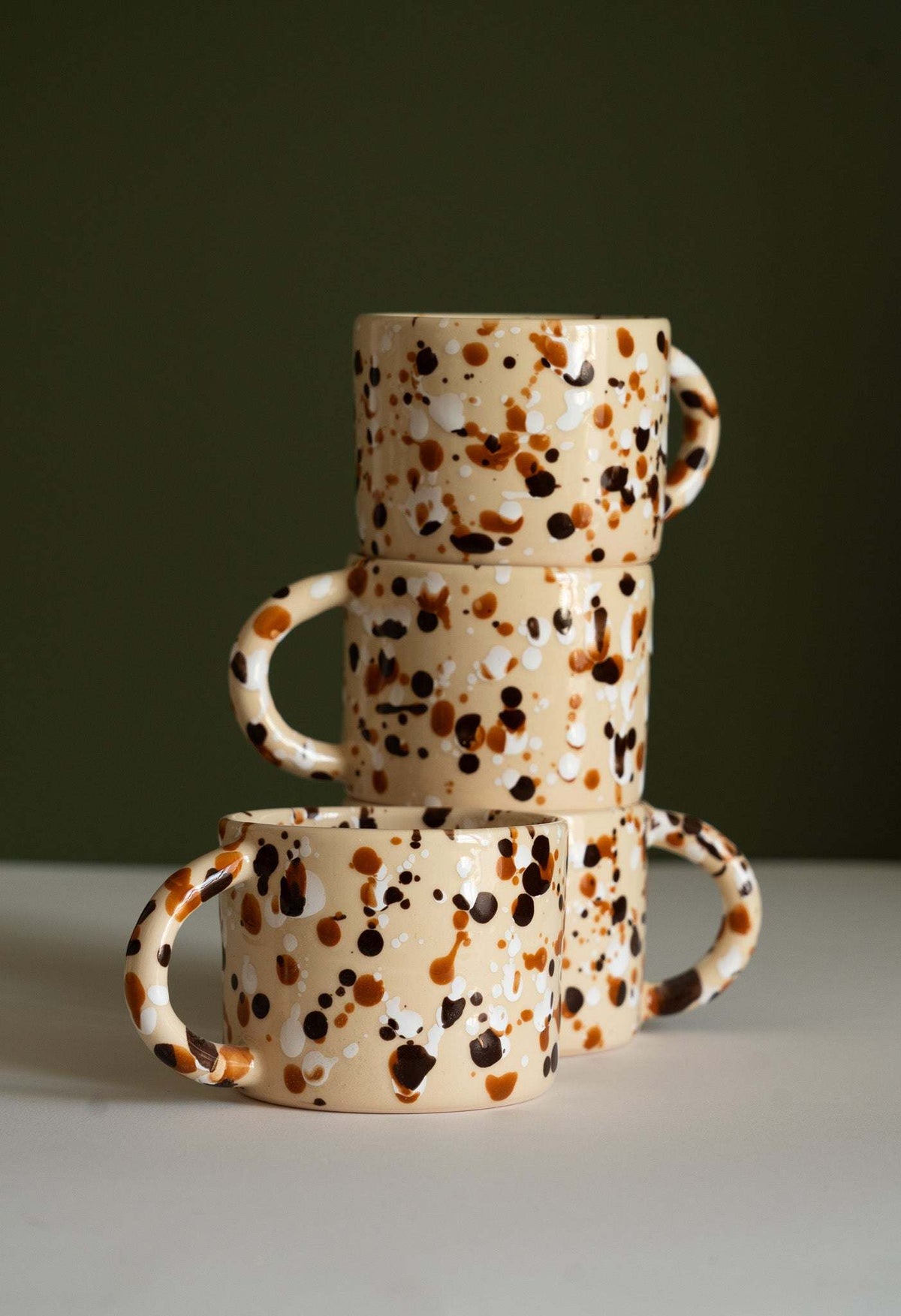 Splatter Stoneware Mug with a glossy cream ceramic finish, covered in brown and black splashes, with a rounded handle
