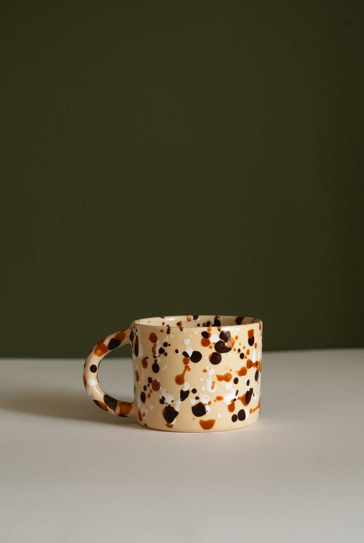 Splatter Stoneware Mug in cream ceramic with irregular brown, black, and orange spots and a rounded handle.