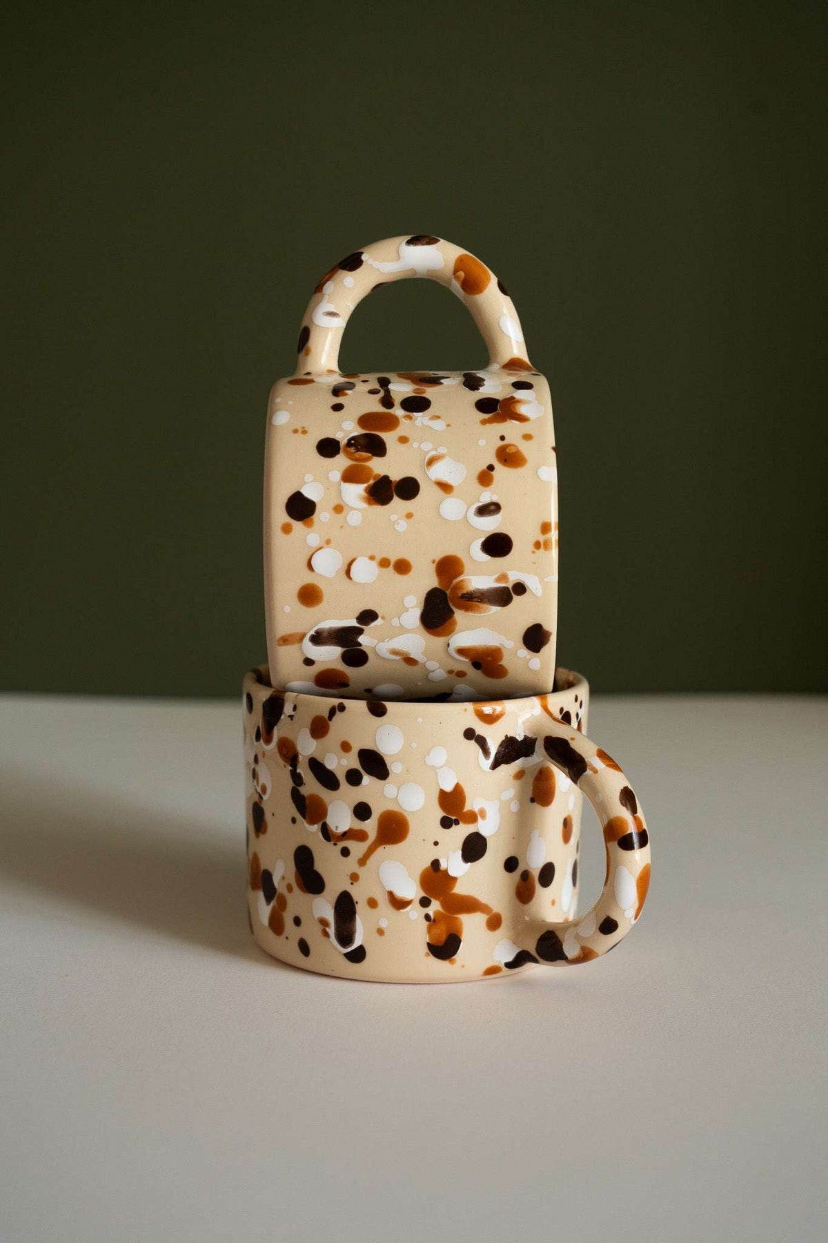 Splatter Stoneware Mug in cream ceramic with glossy caramel, dark brown, and white spots and a rounded handle.
