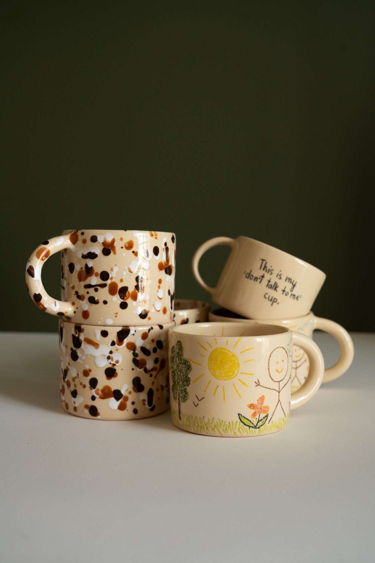 Personalized Stoneware Mug set of four cream ceramic cups with brown speckles and hand-drawn sun, flower, and handwritten designs.