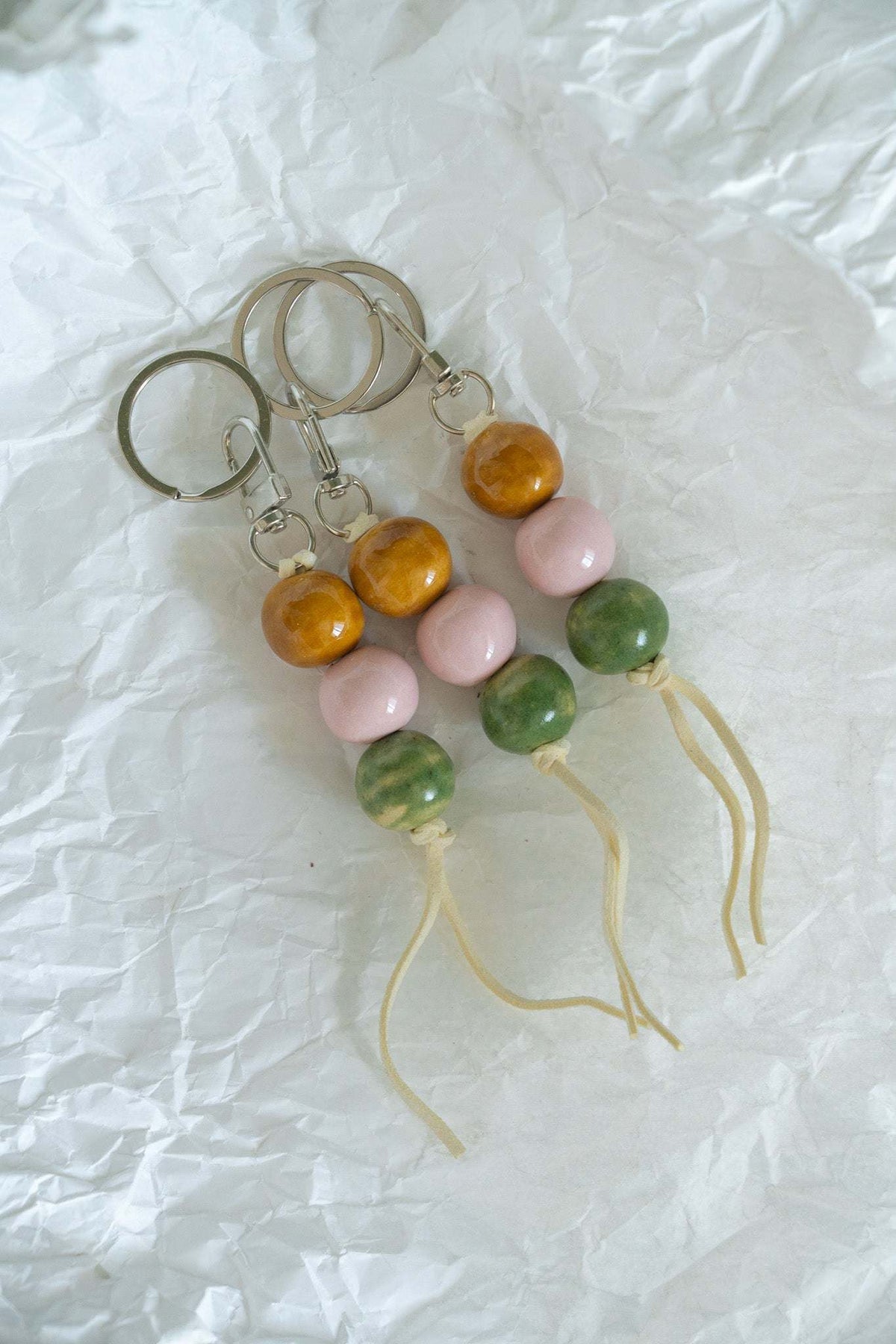 Handmade ceramic keychain with pastel pink, earthy green, and caramel brown beads on leather cord with silver hardware