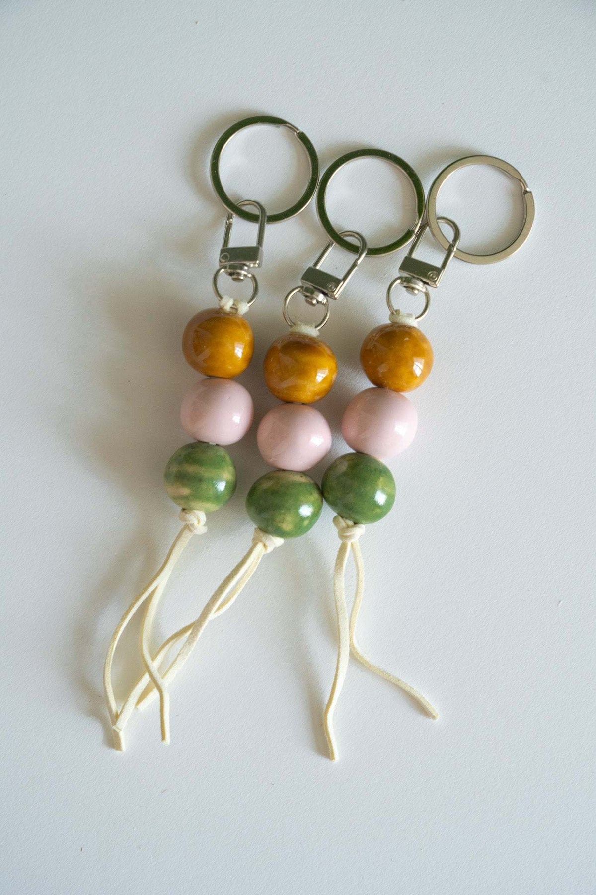 Handmade ceramic keychain with pastel pink, green, and caramel beads on leather cord with silver hardware