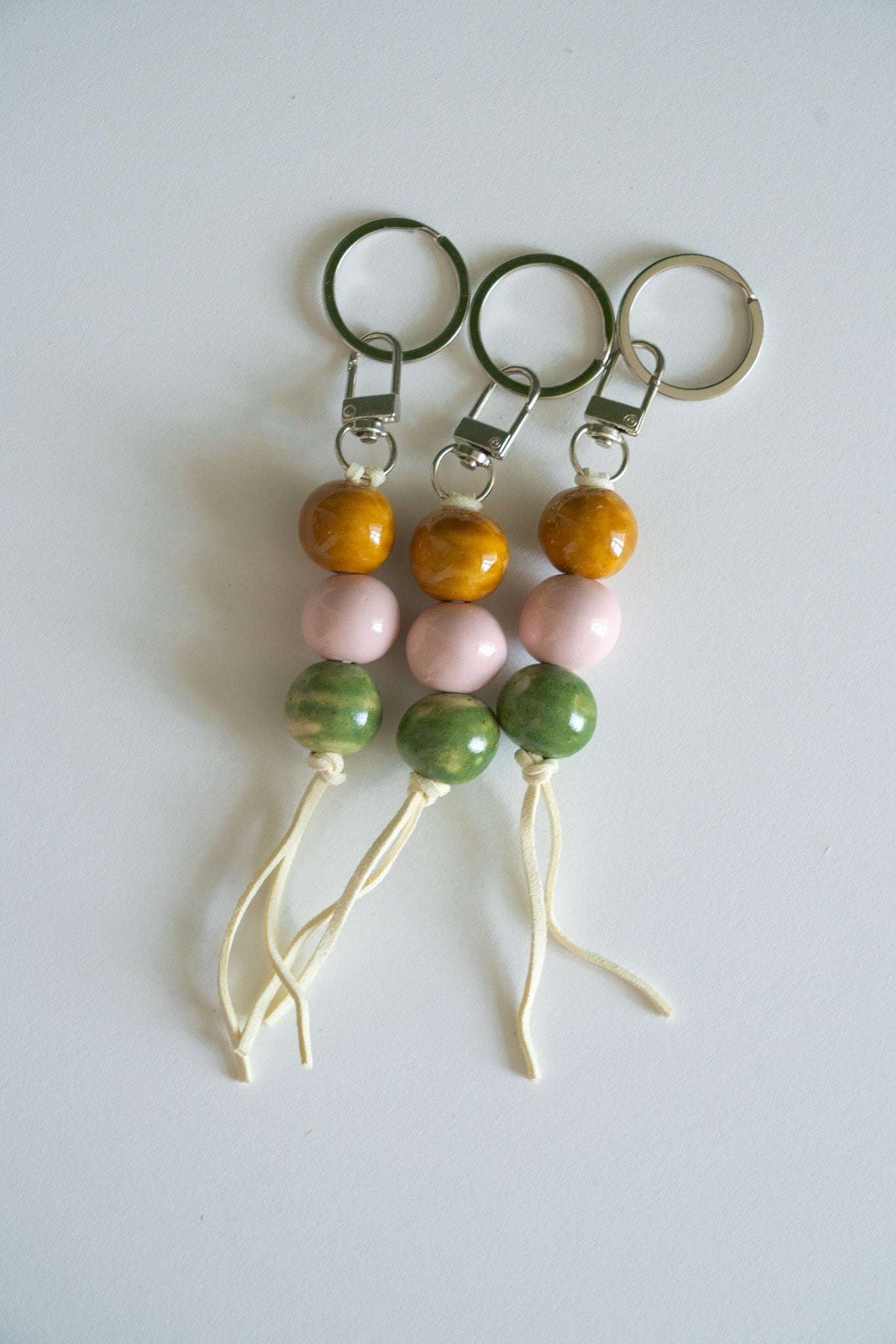 Handmade ceramic keychain with pastel pink, earthy green, and caramel beads on leather cord