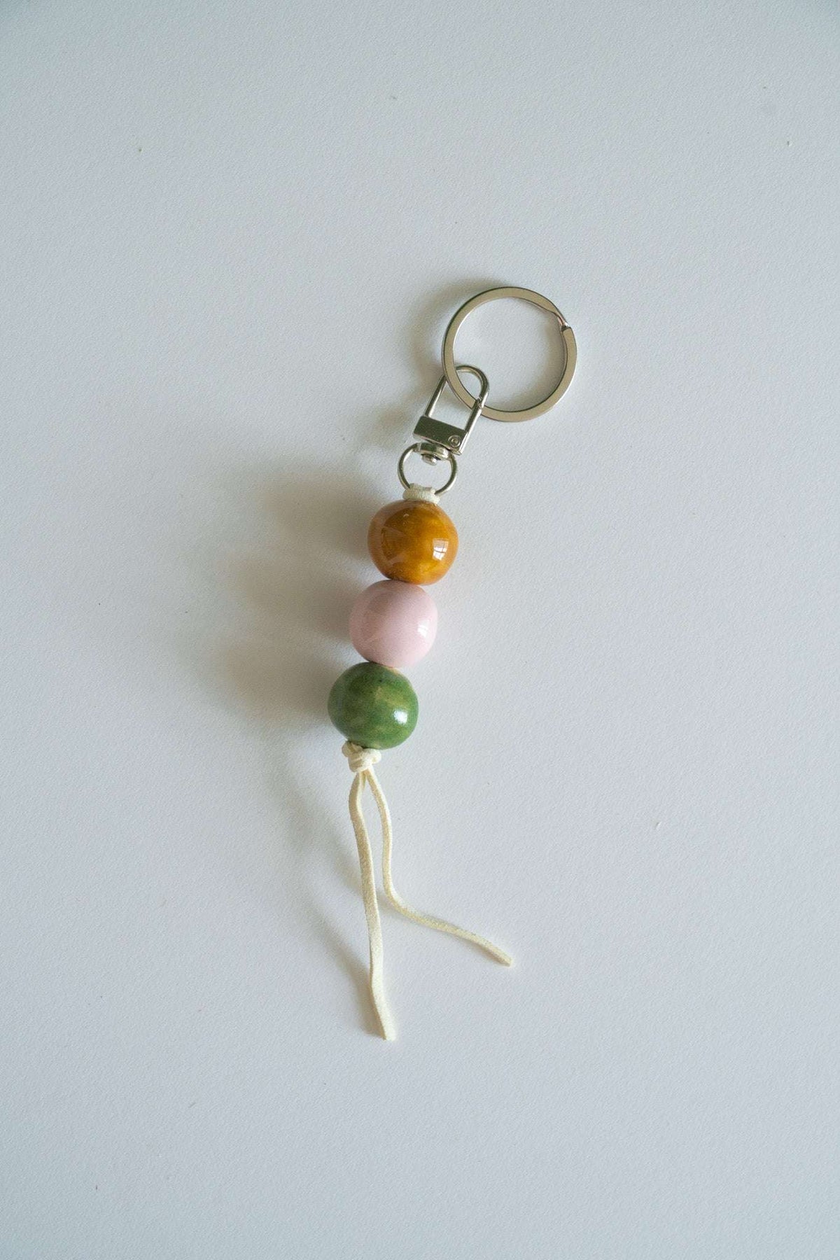 Handmade ceramic keychain with pastel pink, earthy green, and caramel brown beads on leather cord