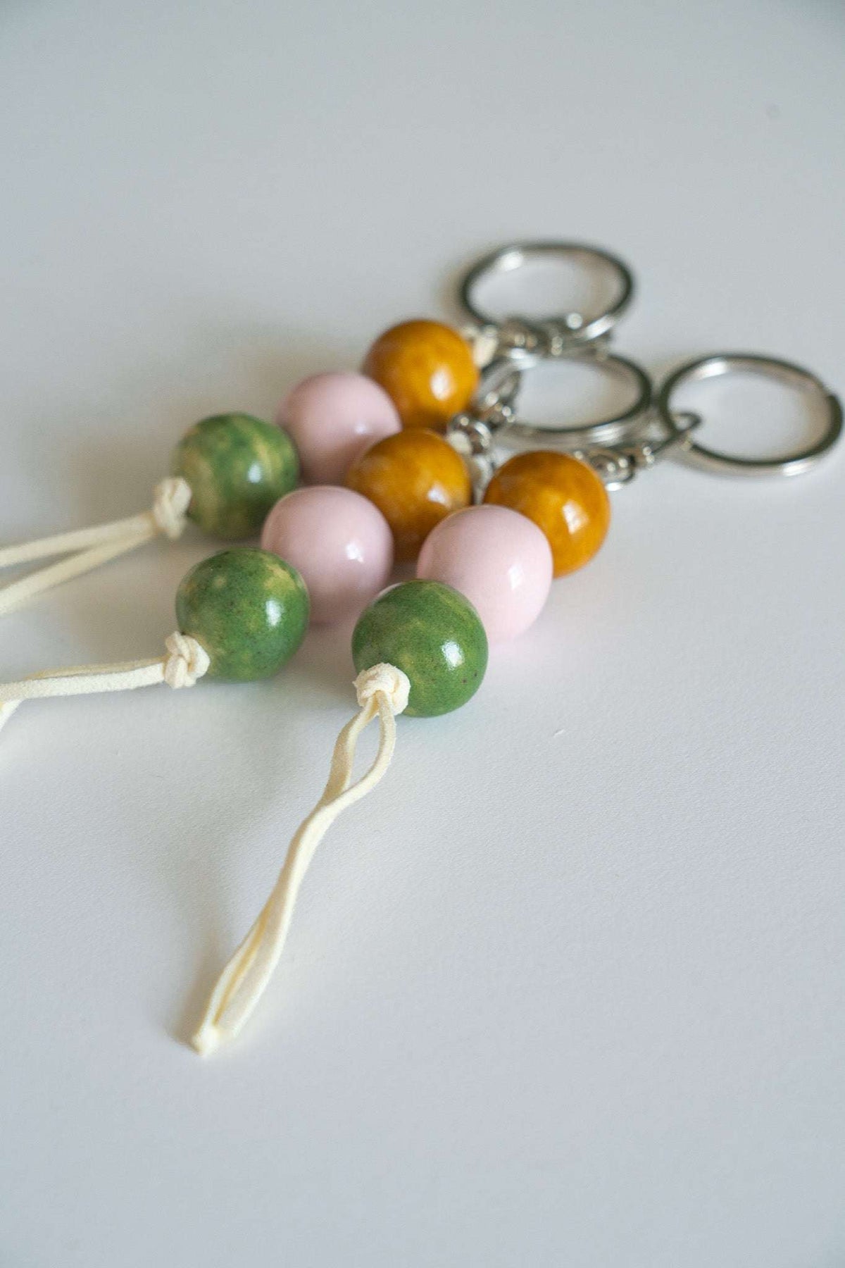 Handmade ceramic keychain with pastel pink, earthy green, and caramel brown beads on leather cord with silver hardware