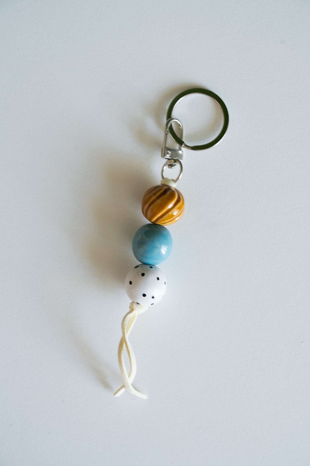 Handmade ceramic keychain with polka dot beads in white, blue, and caramel on leather cord with silver hardware