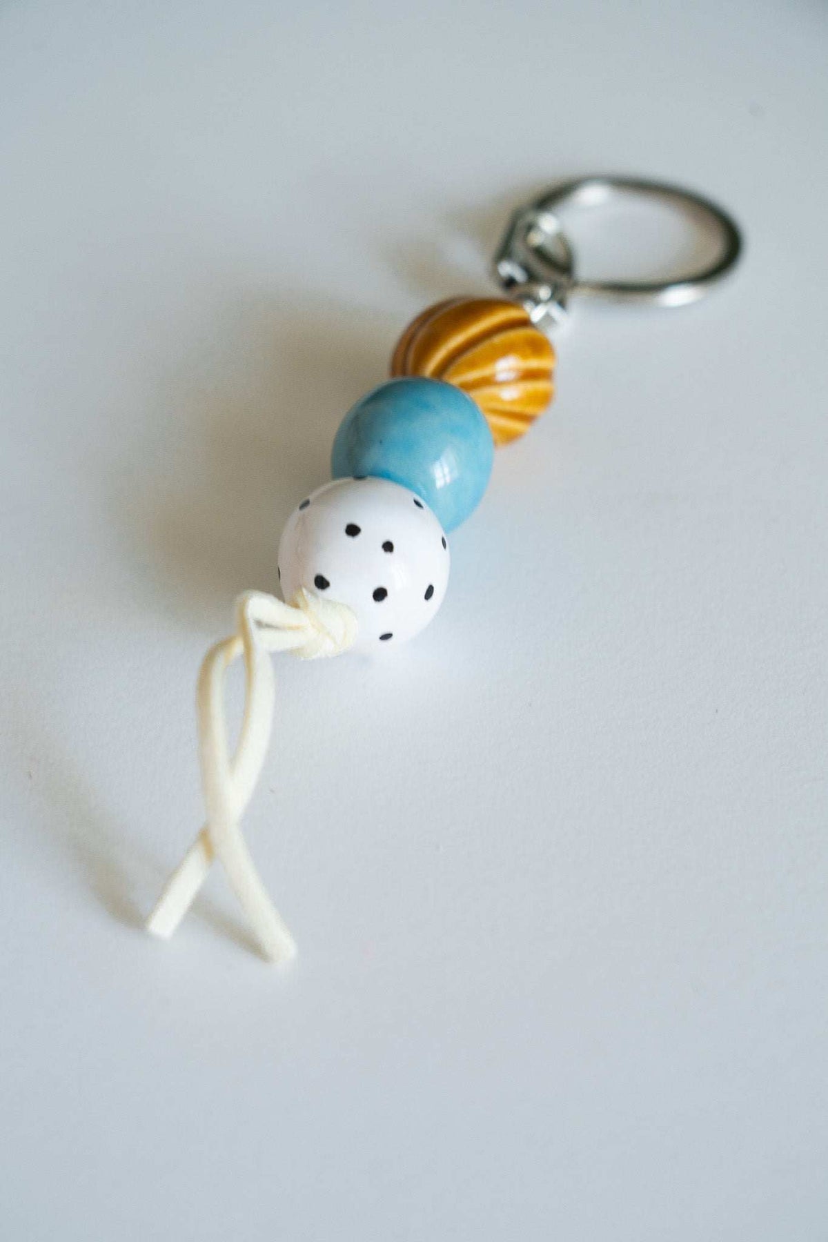Handmade ceramic keychain with three polka dot beads in white, blue, and caramel on leather cord with silver hardware