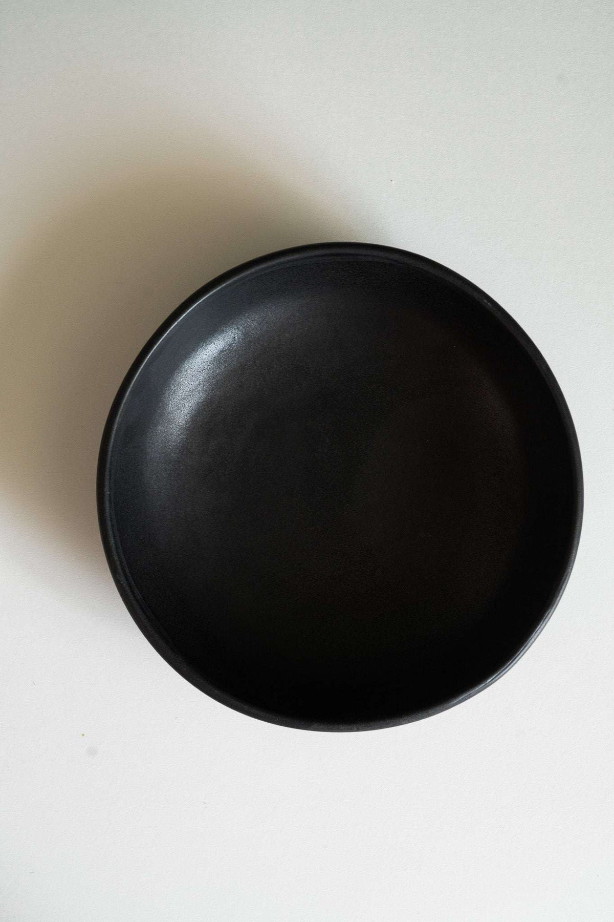 Black stoneware pasta bowl with a smooth matte finish, subtle tonal variation, and a wide, shallow shape.