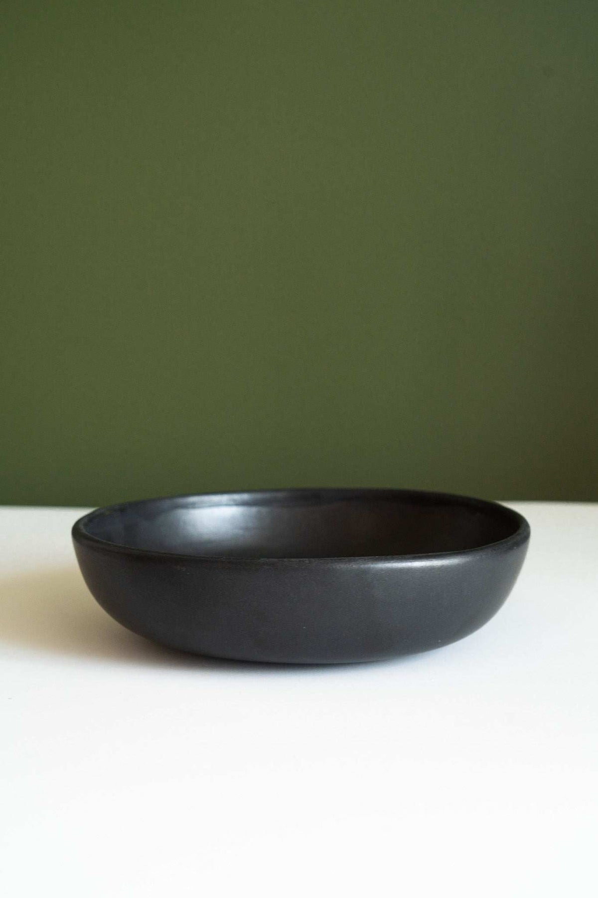 Black matte stoneware pasta bowl with a smooth finish, subtle tonal variation, and a wide, low-profile shape.