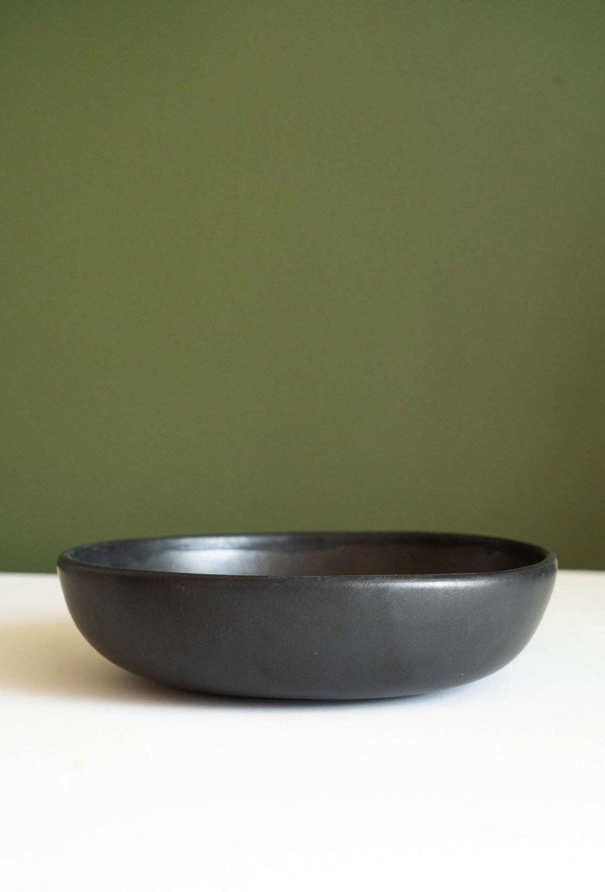 Black stoneware pasta bowl with a smooth matte finish, rounded low-profile shape, and subtly contrasting dark rim.