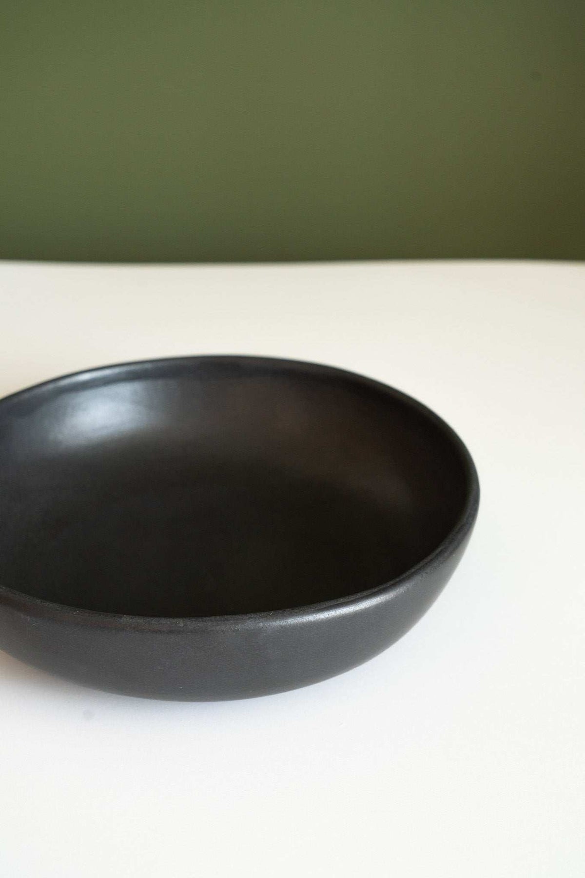 Black stoneware pasta bowl with a smooth matte glaze, shallow open profile, and gently curved rim.