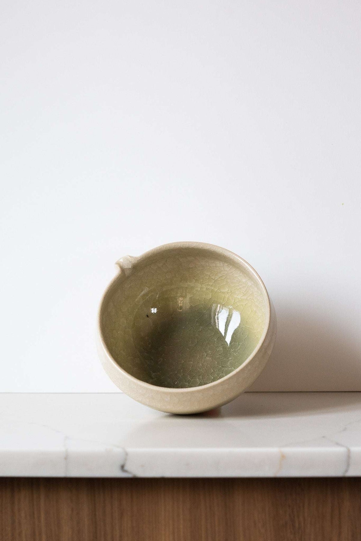 Ceramic Matcha Bowl in sandy cream stoneware with a muted olive-green glazed interior, crackle texture, and pouring spout.