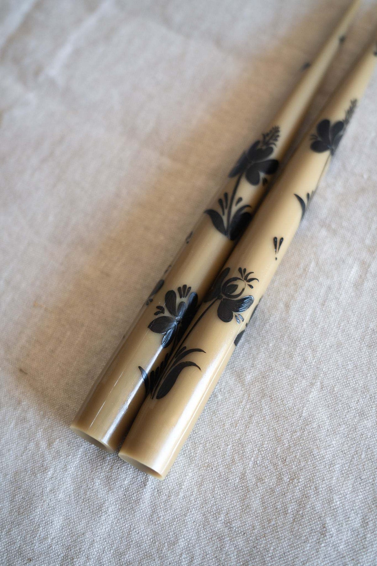 Hand-Painted Taper Candle Set in warm beige wax with black hand-painted floral motifs and slender tapered shape.