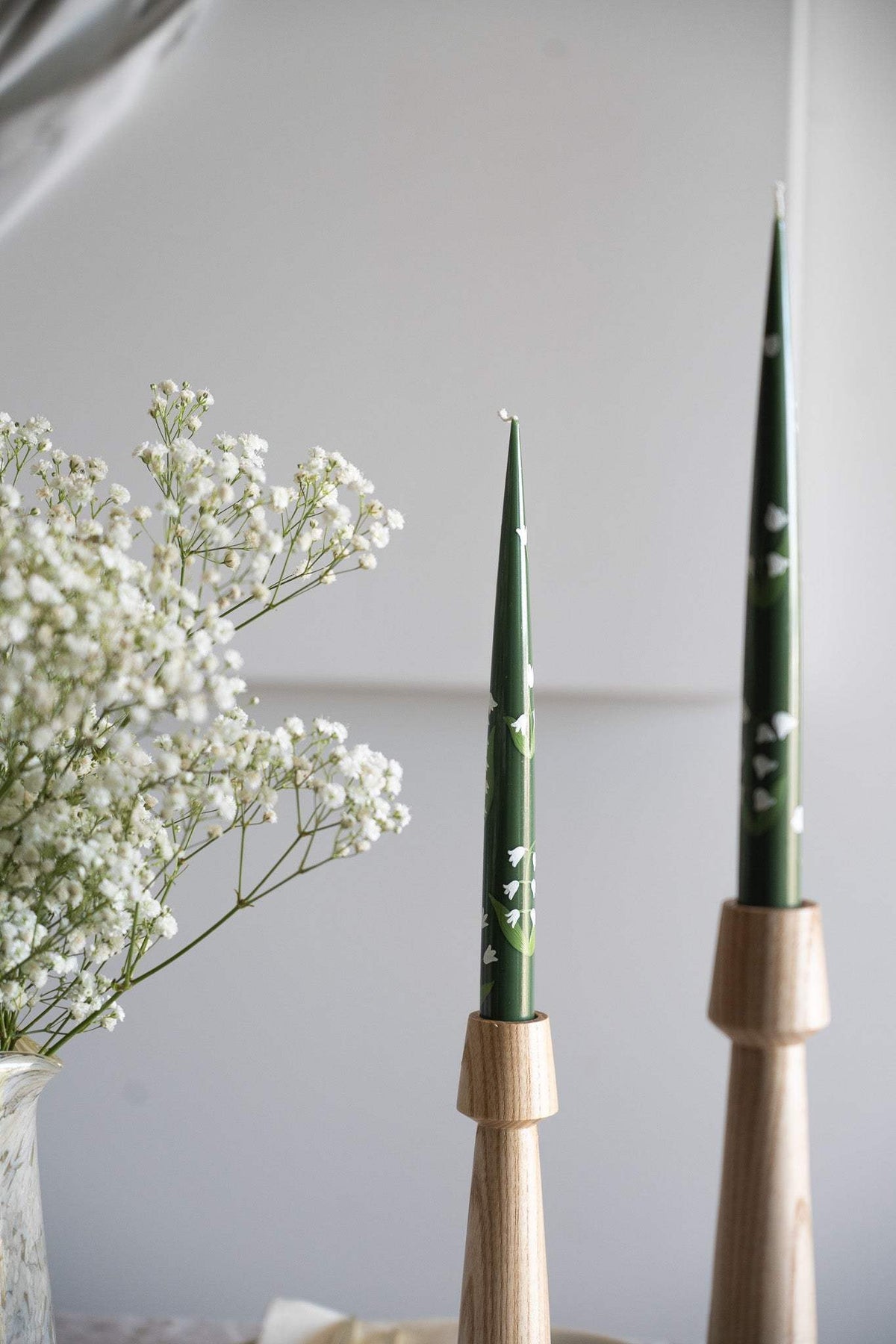 Hand-Painted Taper Candle in deep green with delicate white floral motifs, displayed in natural wood holders.