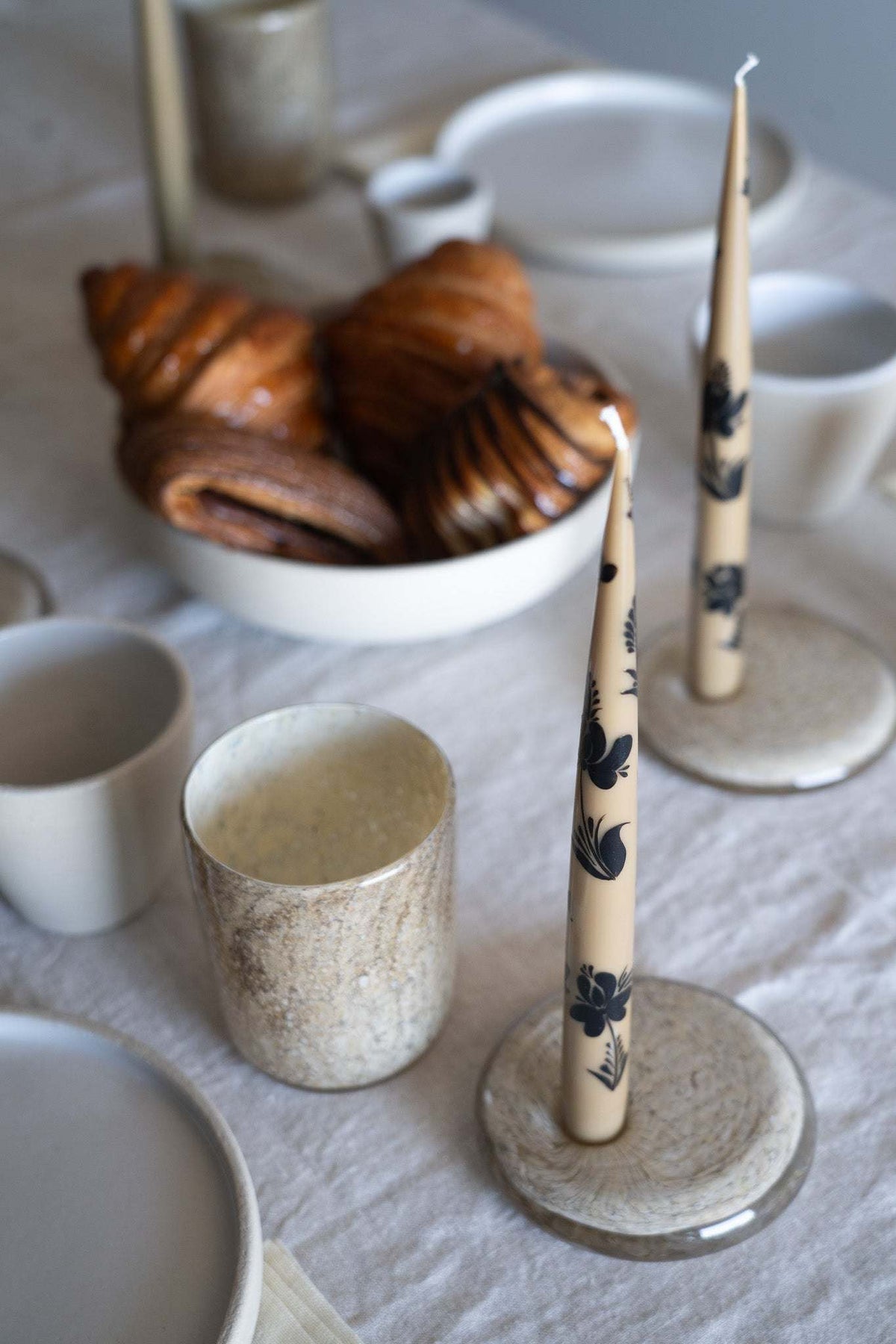 Hand-Painted Taper Candle Set of two cream candles with dark botanical hand-painted motifs in ceramic holders.
