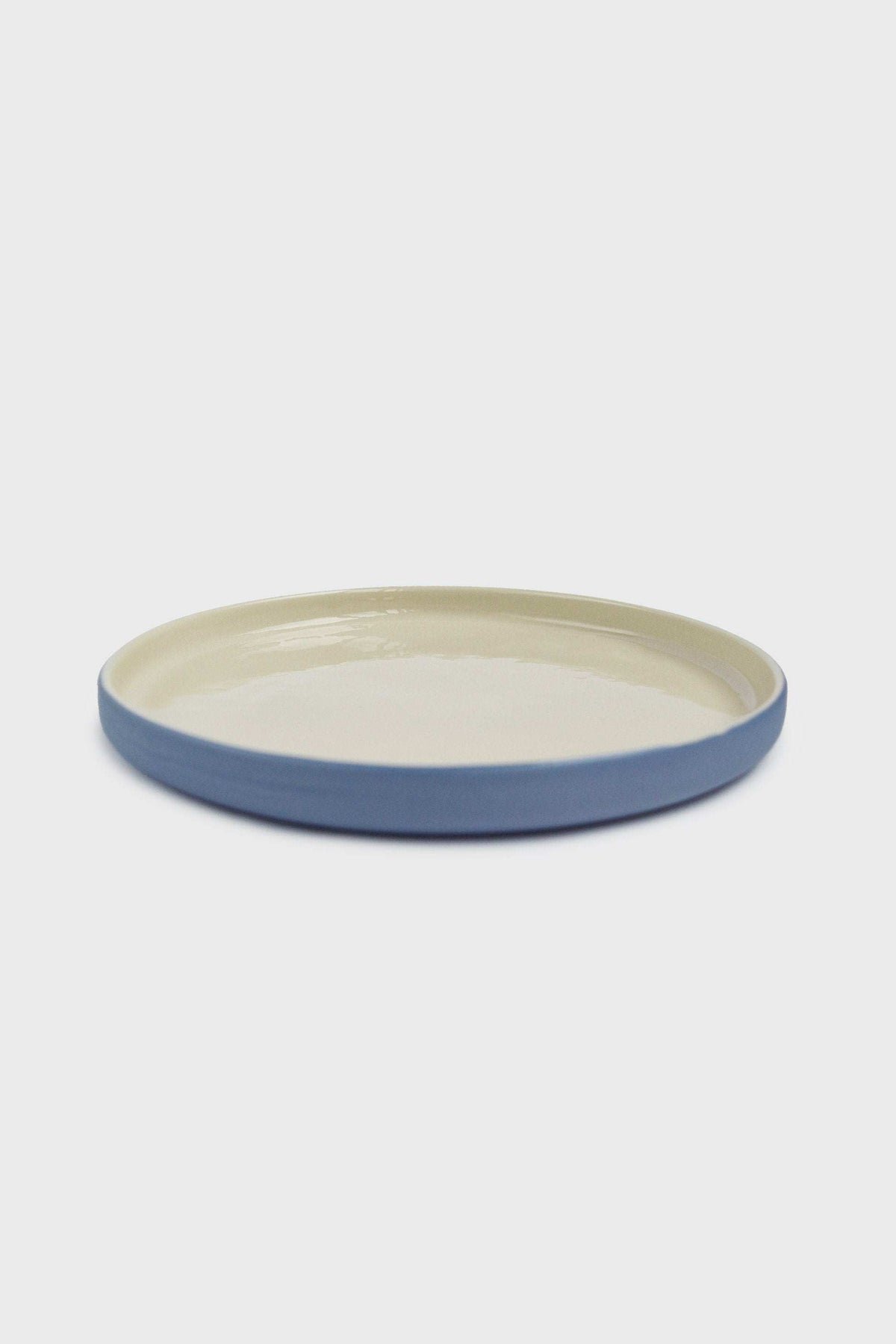 Handmade Blue Porcelain dinner plate with a pale cream glazed interior and solid blue exterior, featuring a low raised rim.