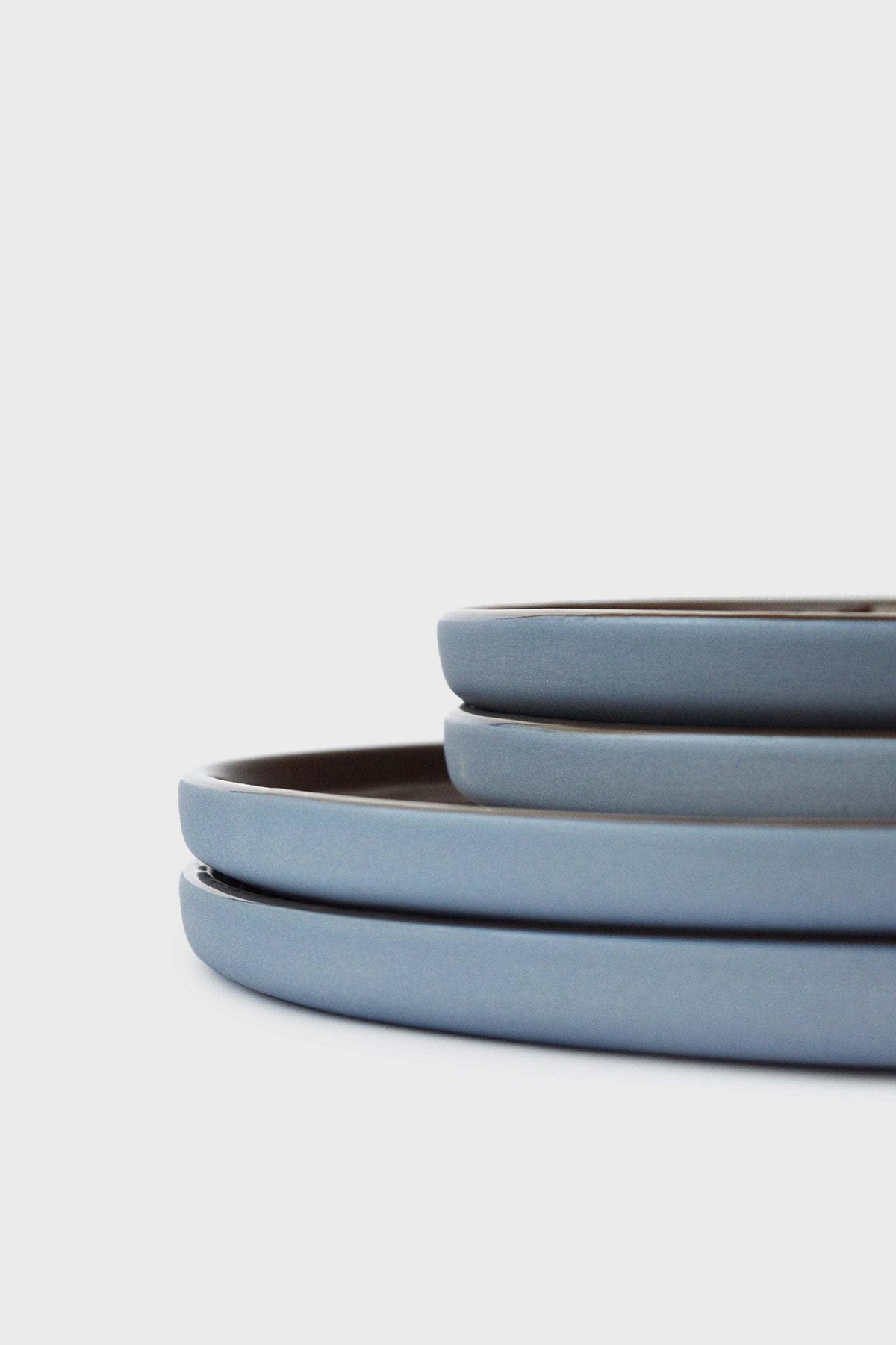 Handmade Blue Porcelain dinner plates in soft blue with smooth glazed surfaces and dark brown interiors, stacked in varying sizes.