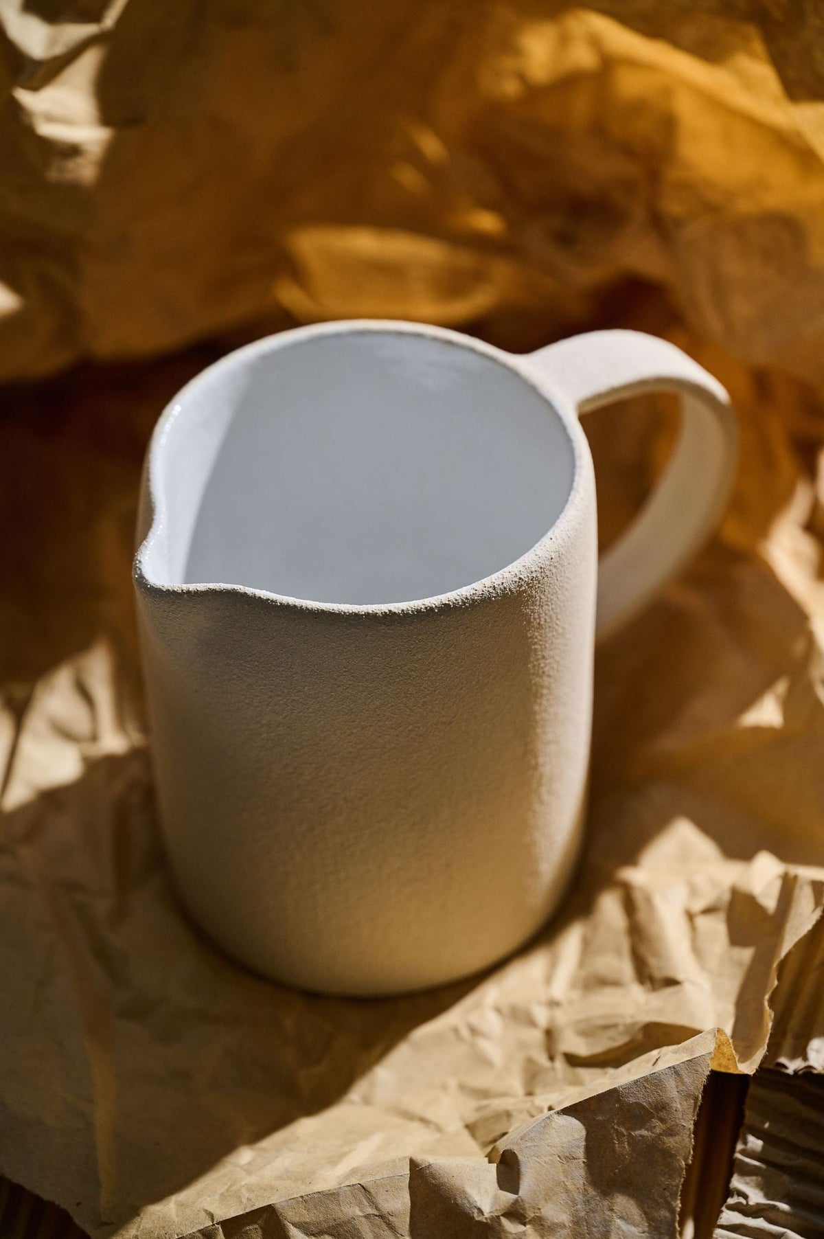 Handmade stoneware pitcher with rough natural exterior and white glazed interior, made in Ukraine