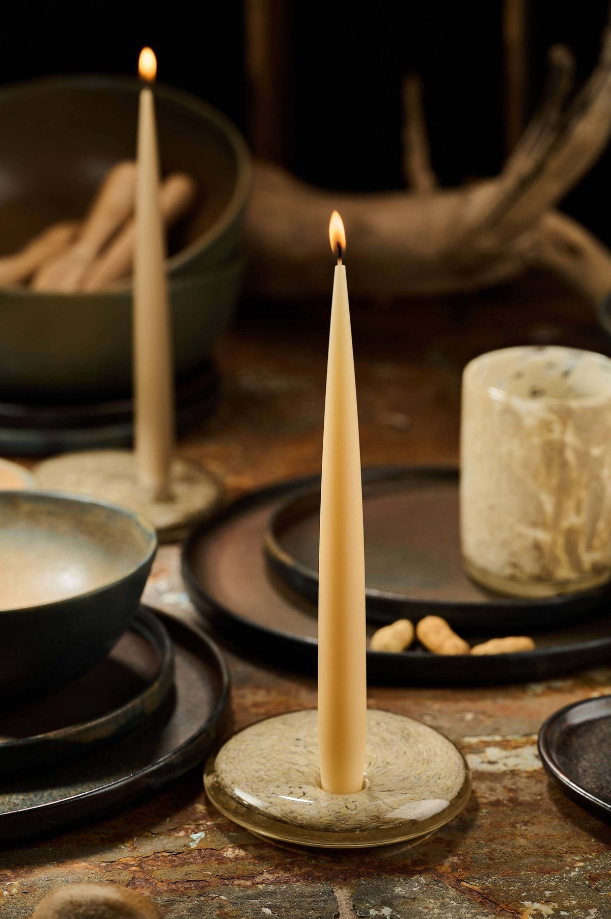 Set of handmade narrow taper candles in four colors displayed in glass holders on a table