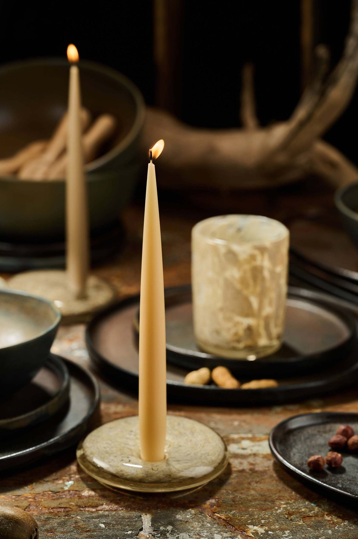 Set of handmade narrow taper candles in four colors displayed in glass holders on a wooden table