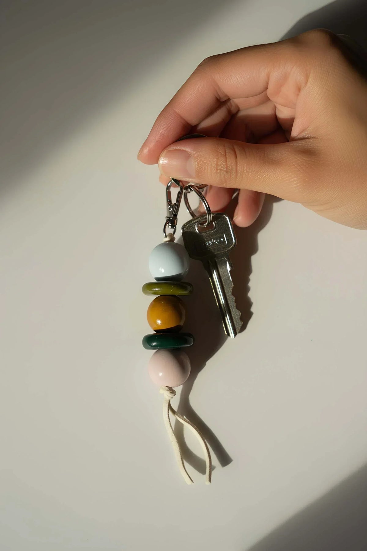 Beaded Keychain with glossy white, ochre, green and blush beads, silver-tone keys and a natural leather cord.