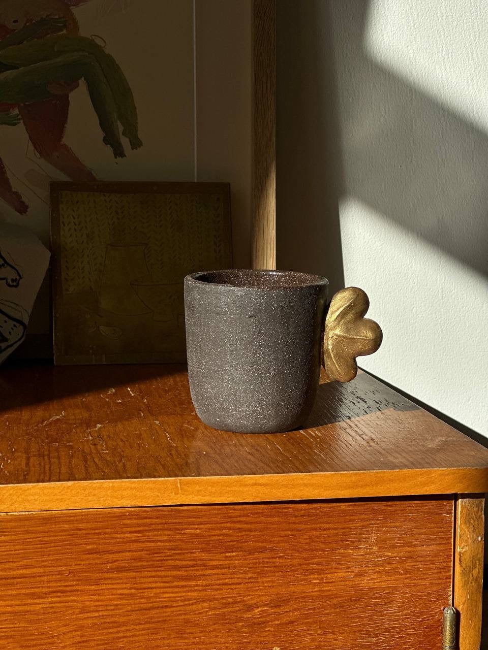 Handmade Stoneware Coffee Cup in charcoal gray with a rough matte exterior, dark glazed interior, and gold leaf accent.