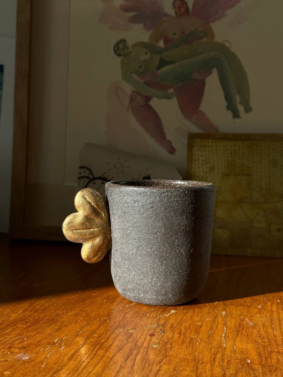 Handmade Stoneware Coffee Cup in dark gray, with a rough speckled finish and a sculpted gold leaf handle accent.
