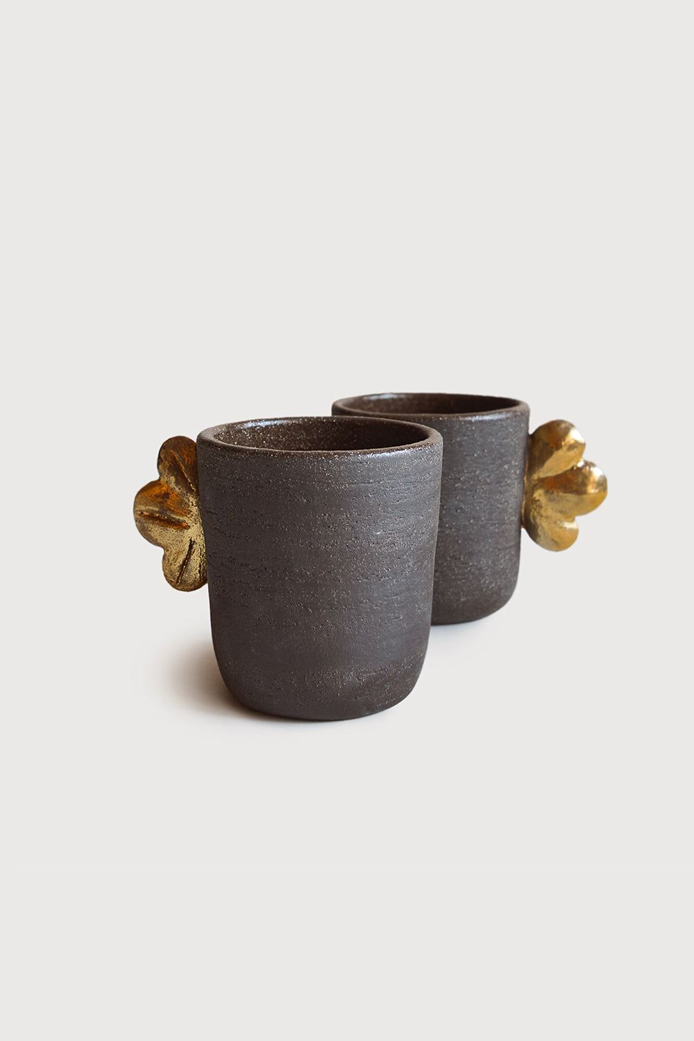 Handmade Stoneware Coffee Cup in dark brown-gray textured stoneware, with a rough matte finish and sculpted gold leaf handles.