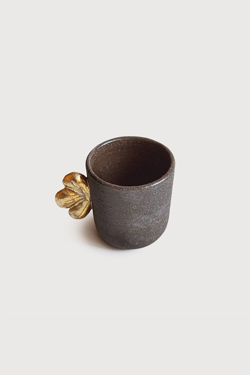 Handmade Stoneware Coffee Cup in dark charcoal-brown with a rough matte exterior and gold leaf-shaped handle detail
