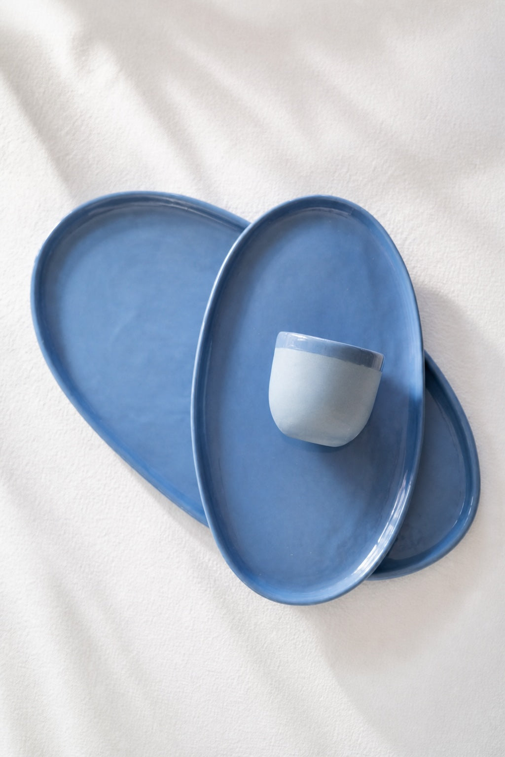 Oval Serving Platter set in glossy blue porcelain, with softly irregular edges and a matching small cup nestled on top.