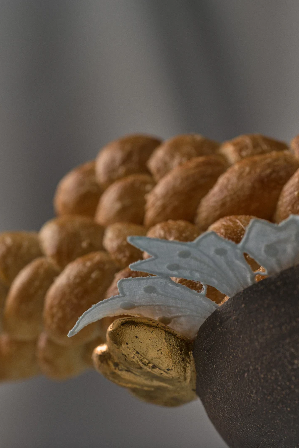 Pedestal fruit bowl in dark brown textured stoneware, with sculpted gold leaves and a rounded fruit-like detail.