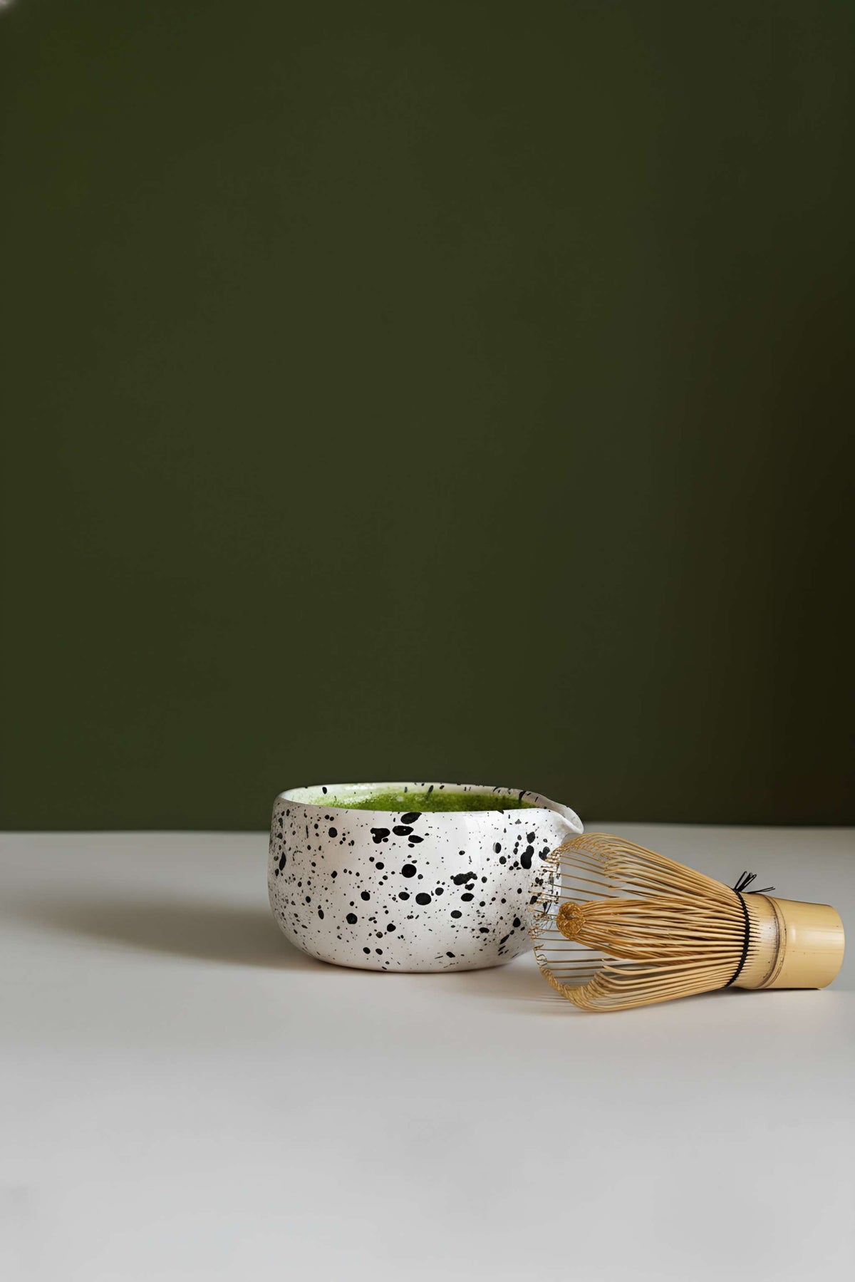 Handmade Matcha Bowl in white stoneware with black speckles, paired with a bamboo whisk and golden handle.