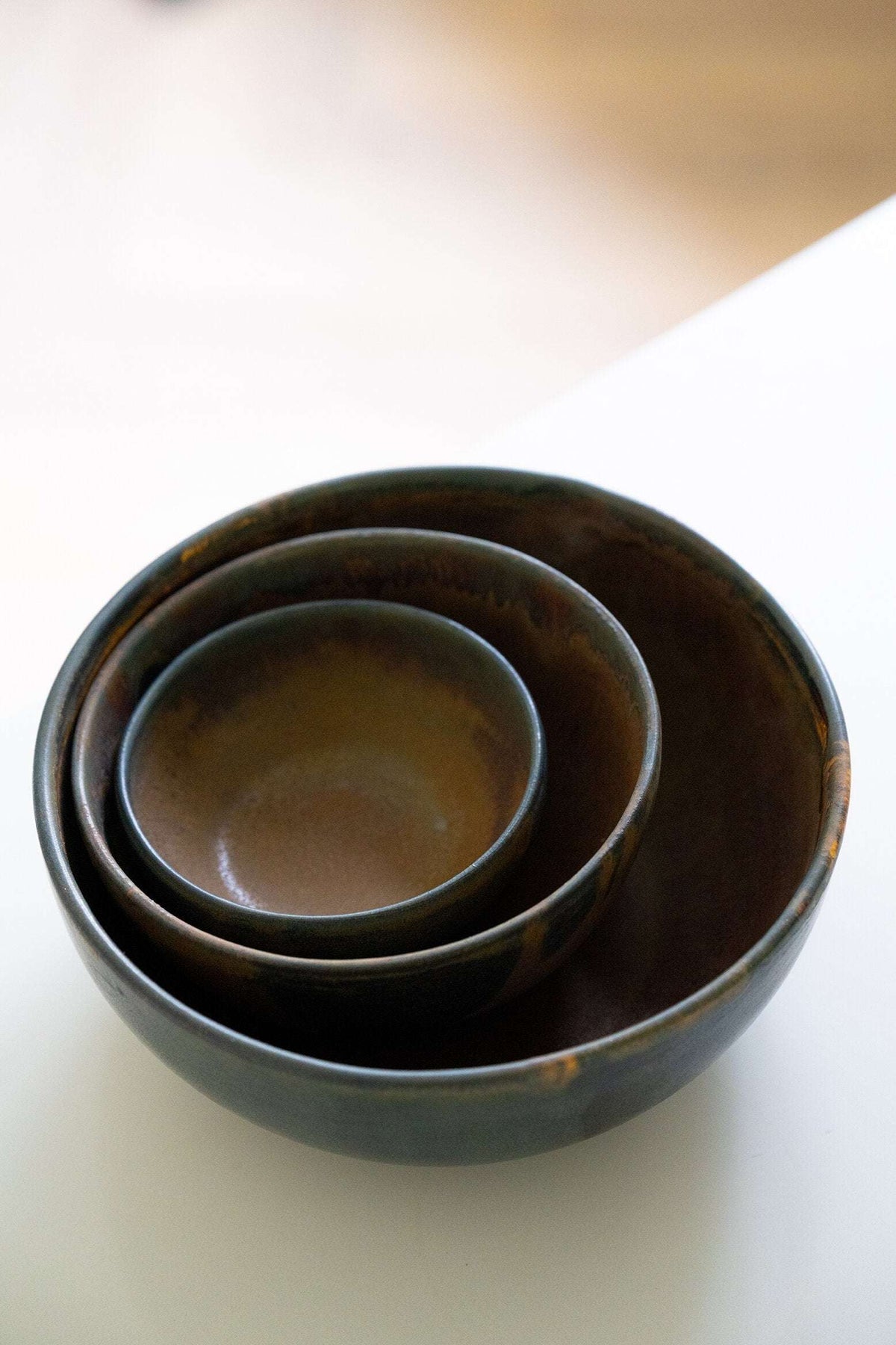 Rust stoneware nesting bowl set with matte brown-black reactive glaze and subtle swirls