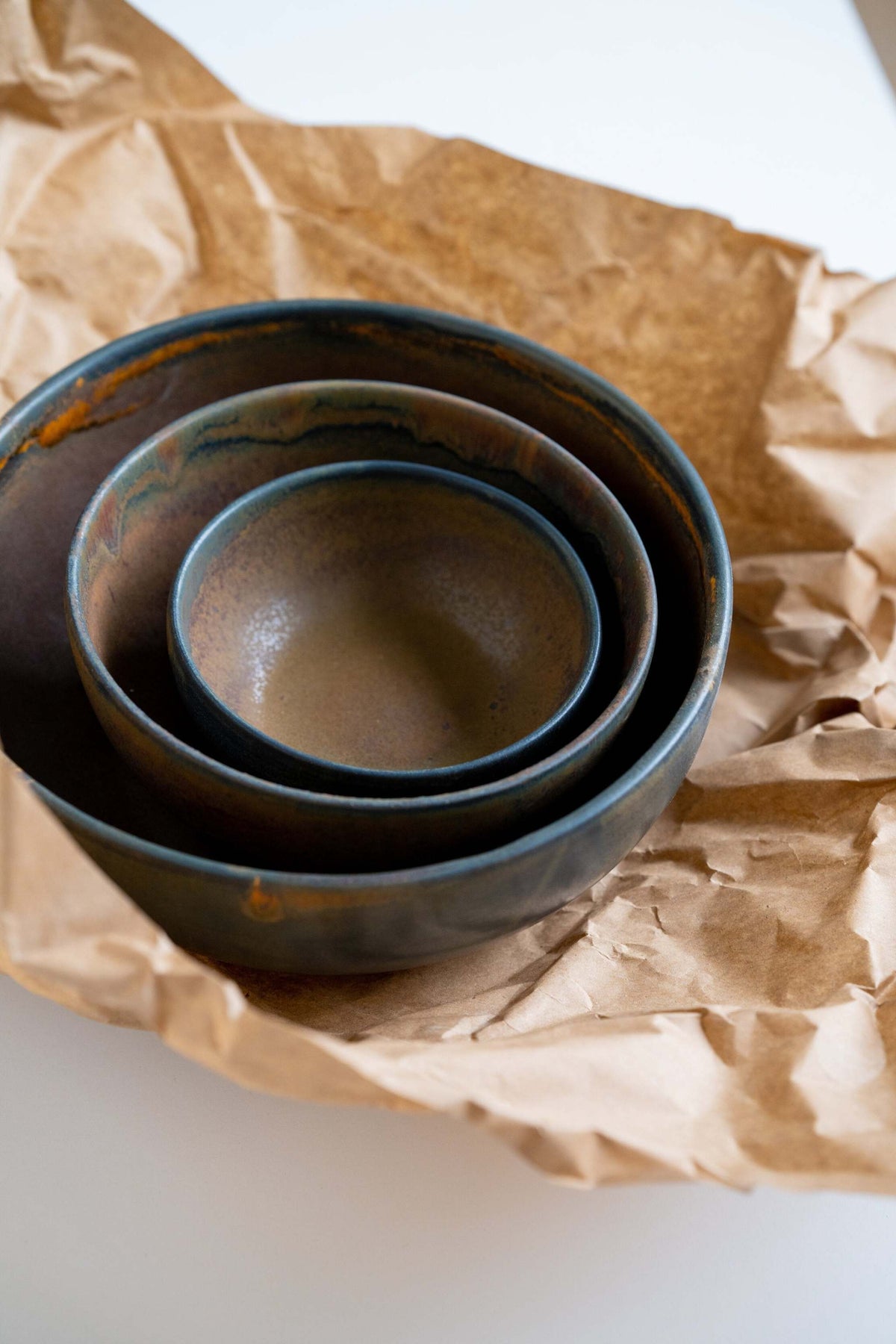 Rust stoneware nesting bowl set with matte brown-black reactive glaze and subtle swirl patterns