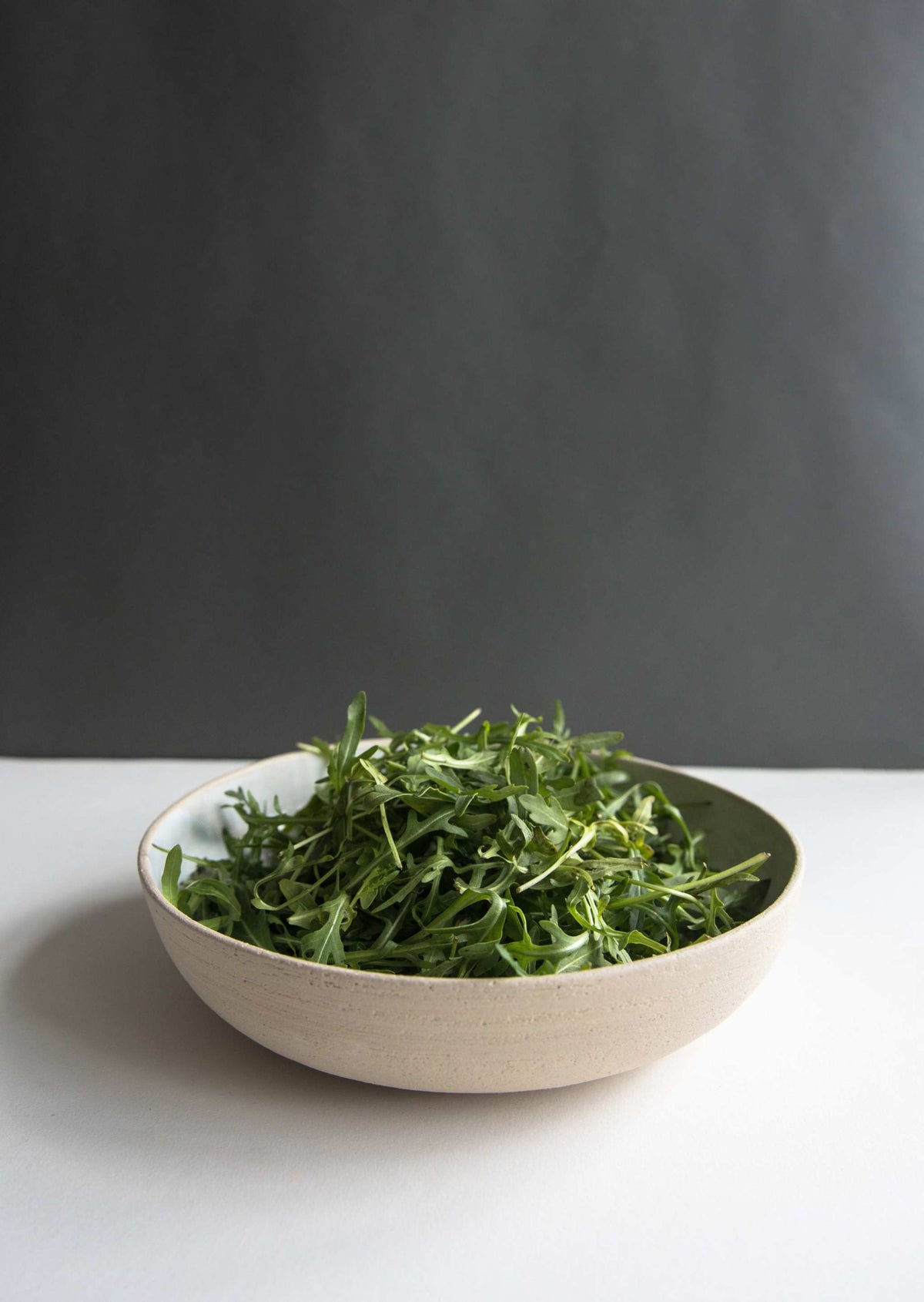 Stoneware Pasta Bowl with a pale cream, speckled stoneware exterior, white glazed interior, and gently rounded shape.
