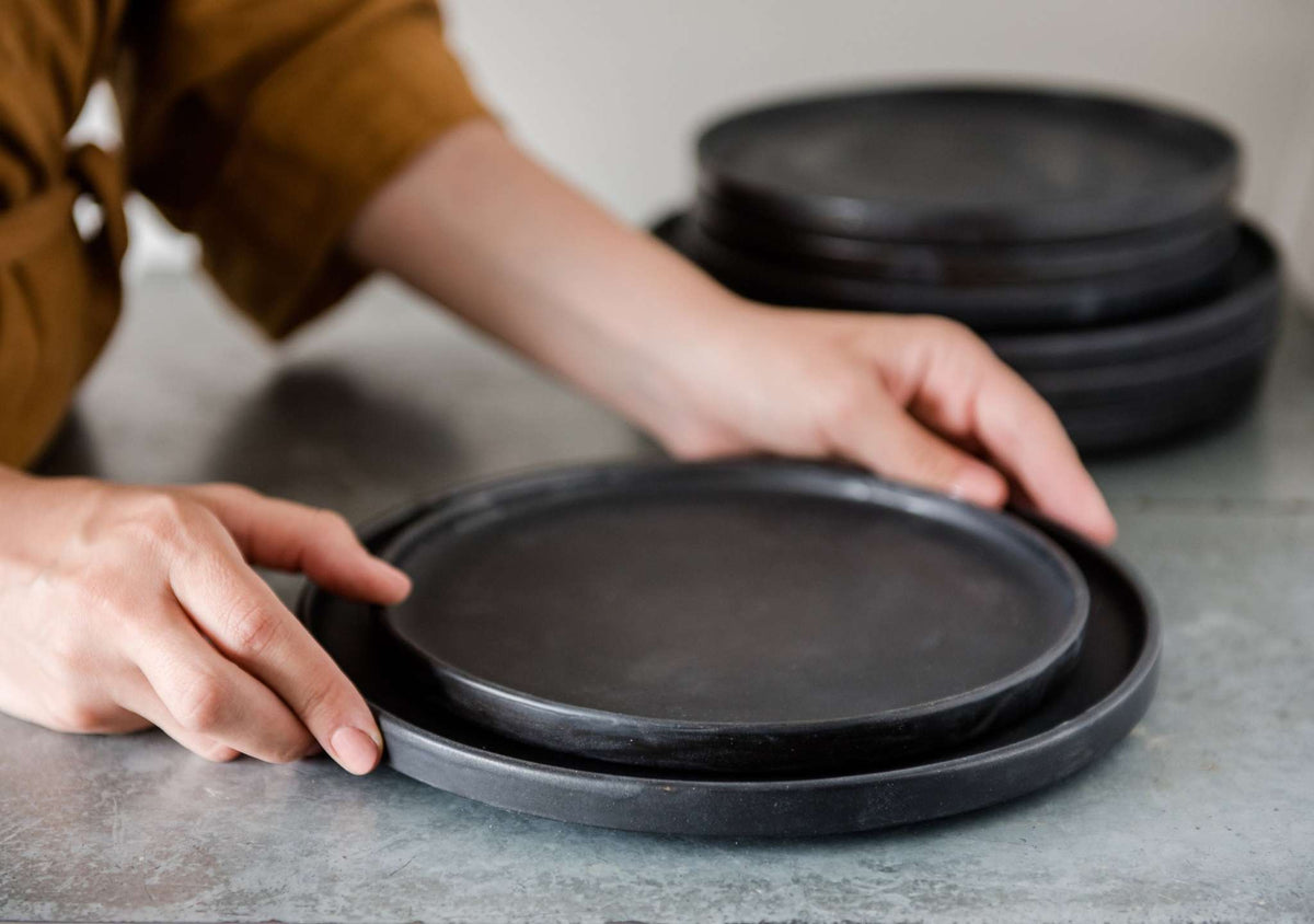 Black matte stoneware dinner plate with textured glaze and light border ring, handmade in Ukraine